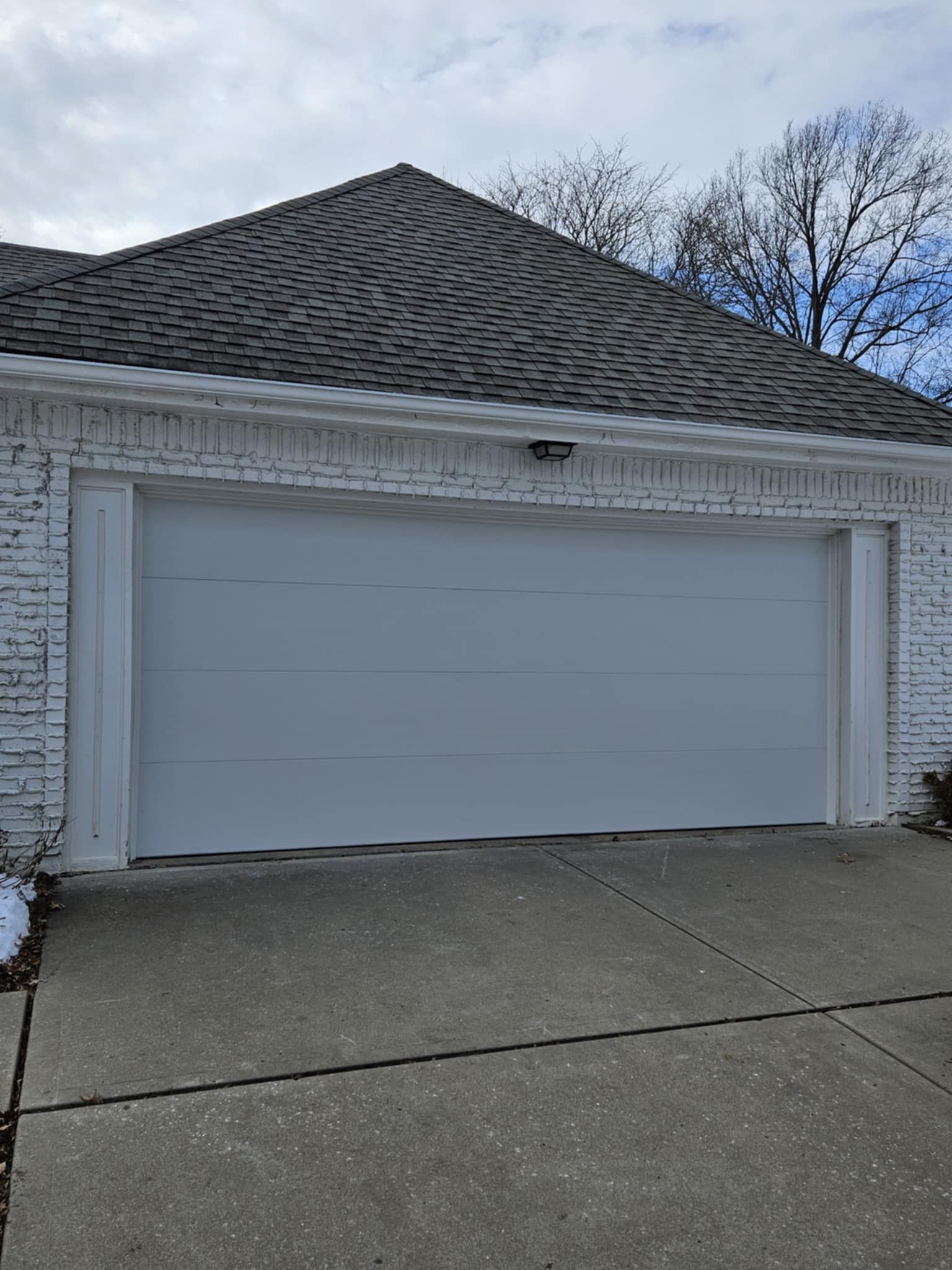 A white garage door is sitting in front of a white brick house.
