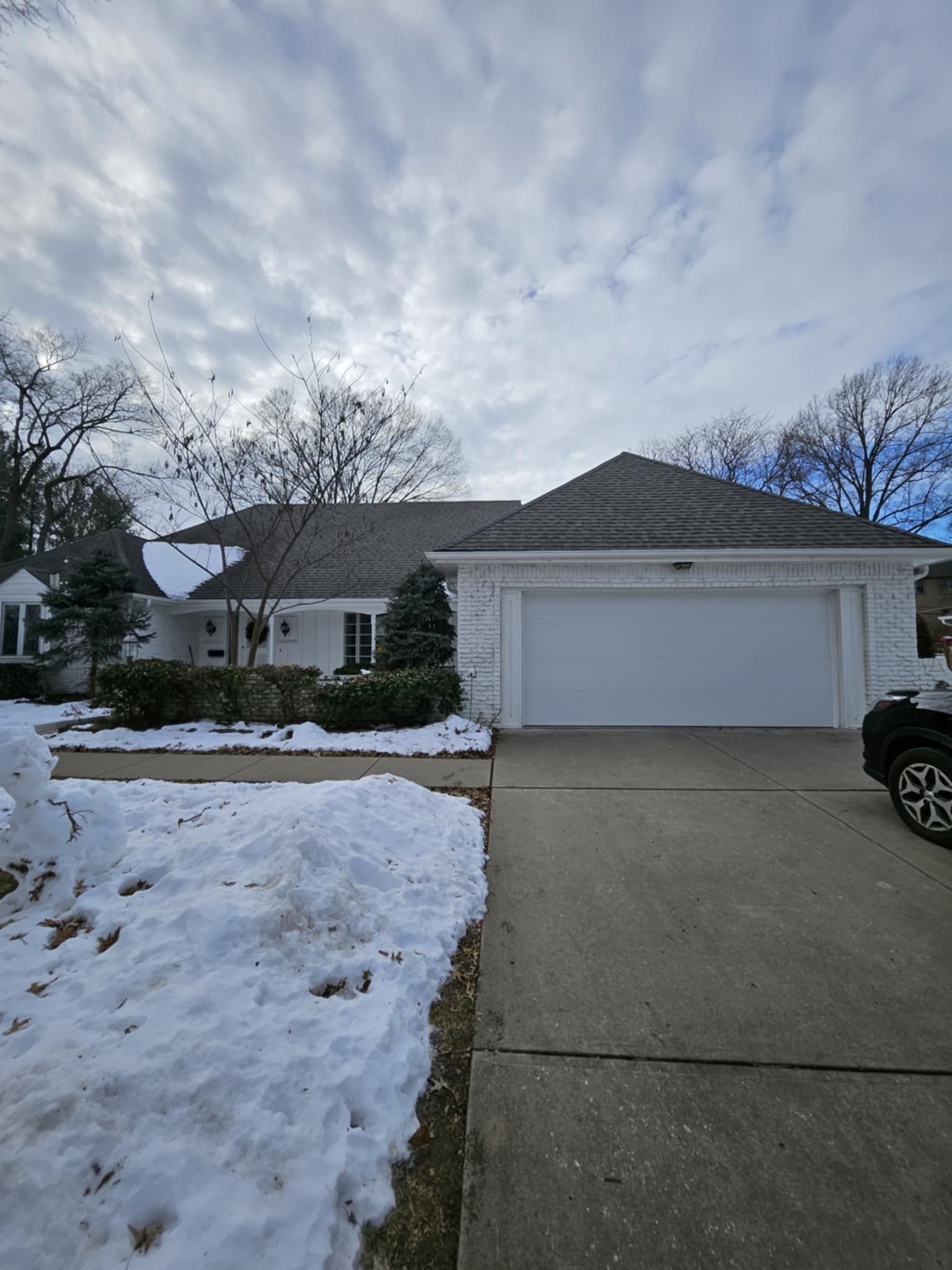 A car is parked in front of a house with a garage door.