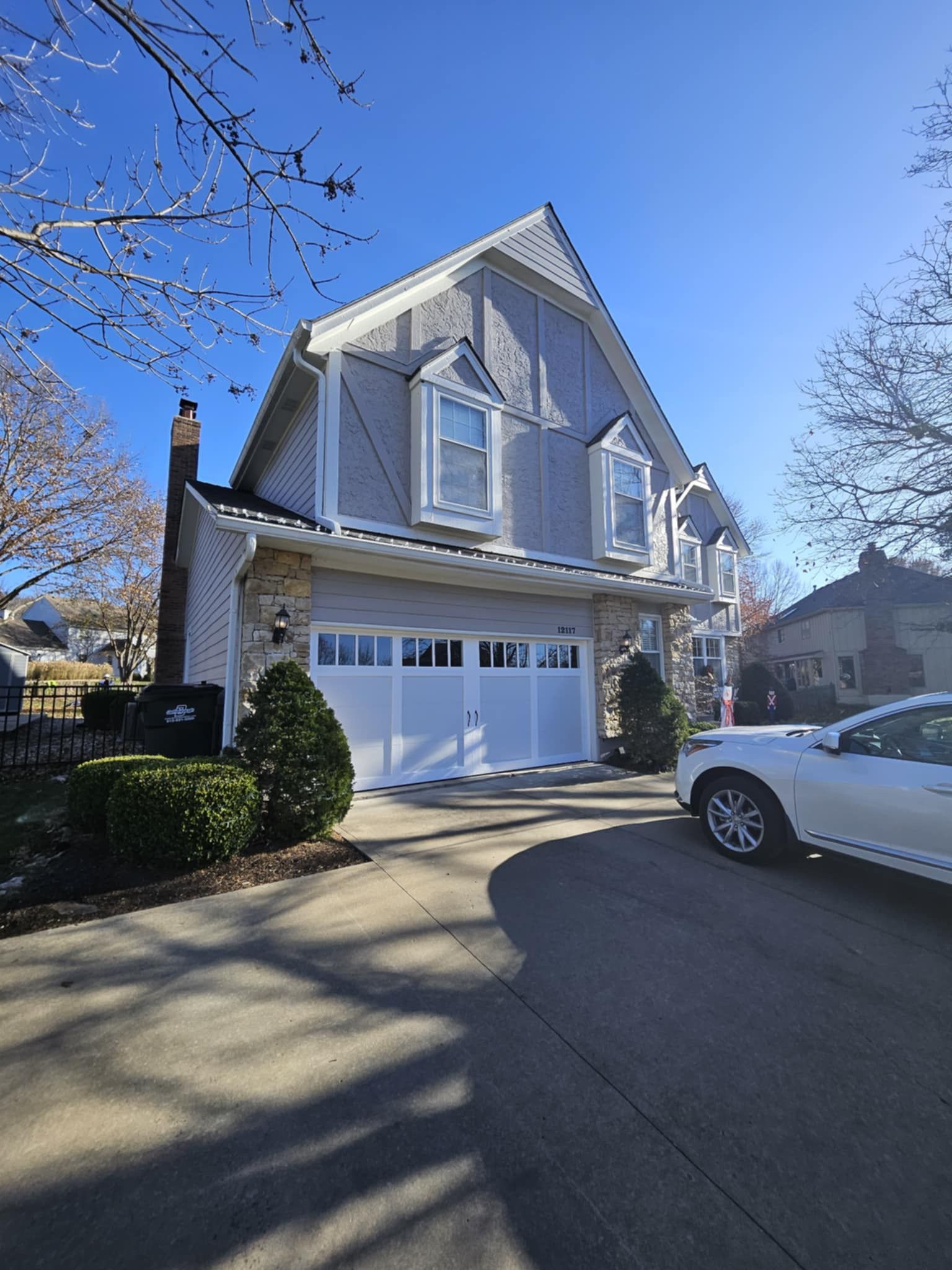 A white car is parked in front of a large house.