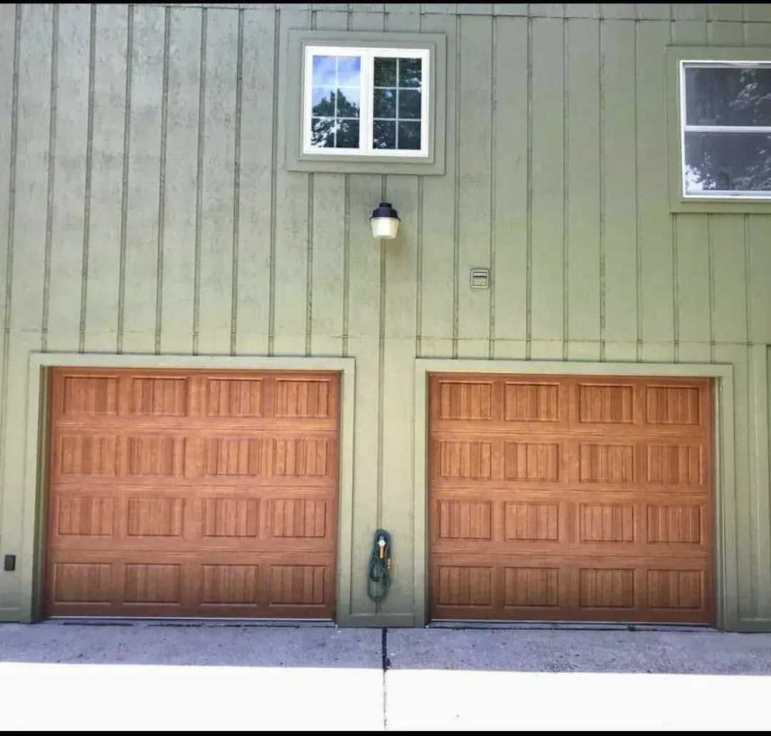 A green house with two brown garage doors and a window