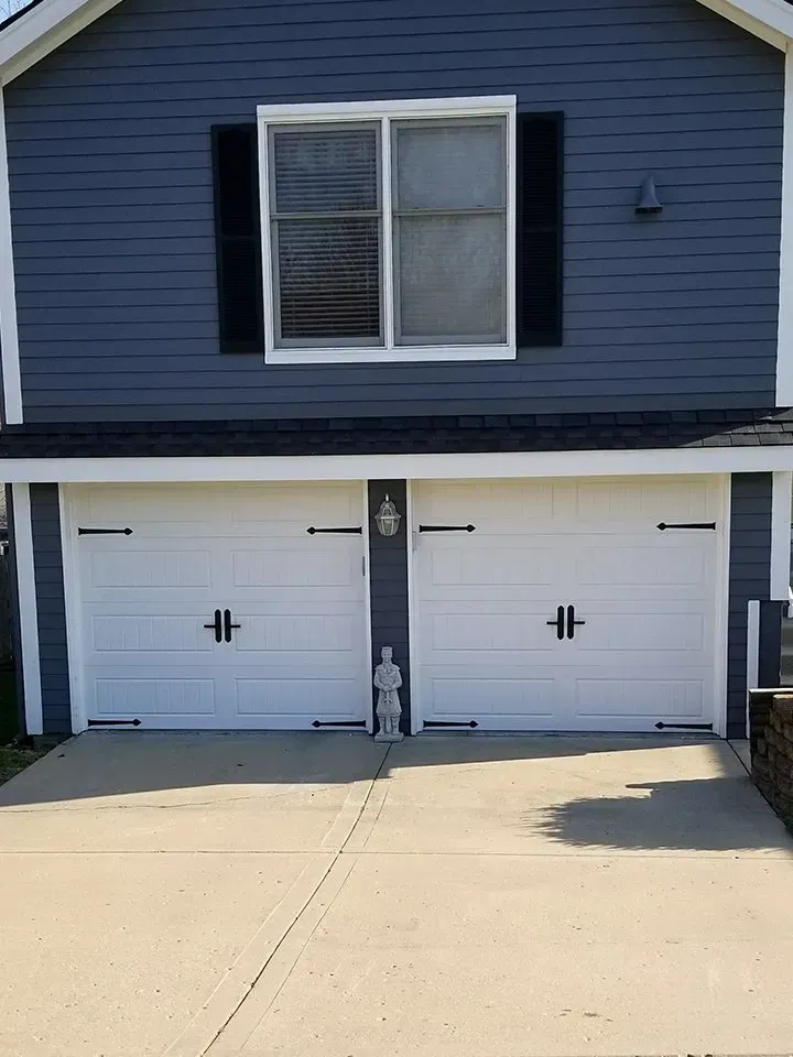 A blue house with two white garage doors and a window.
