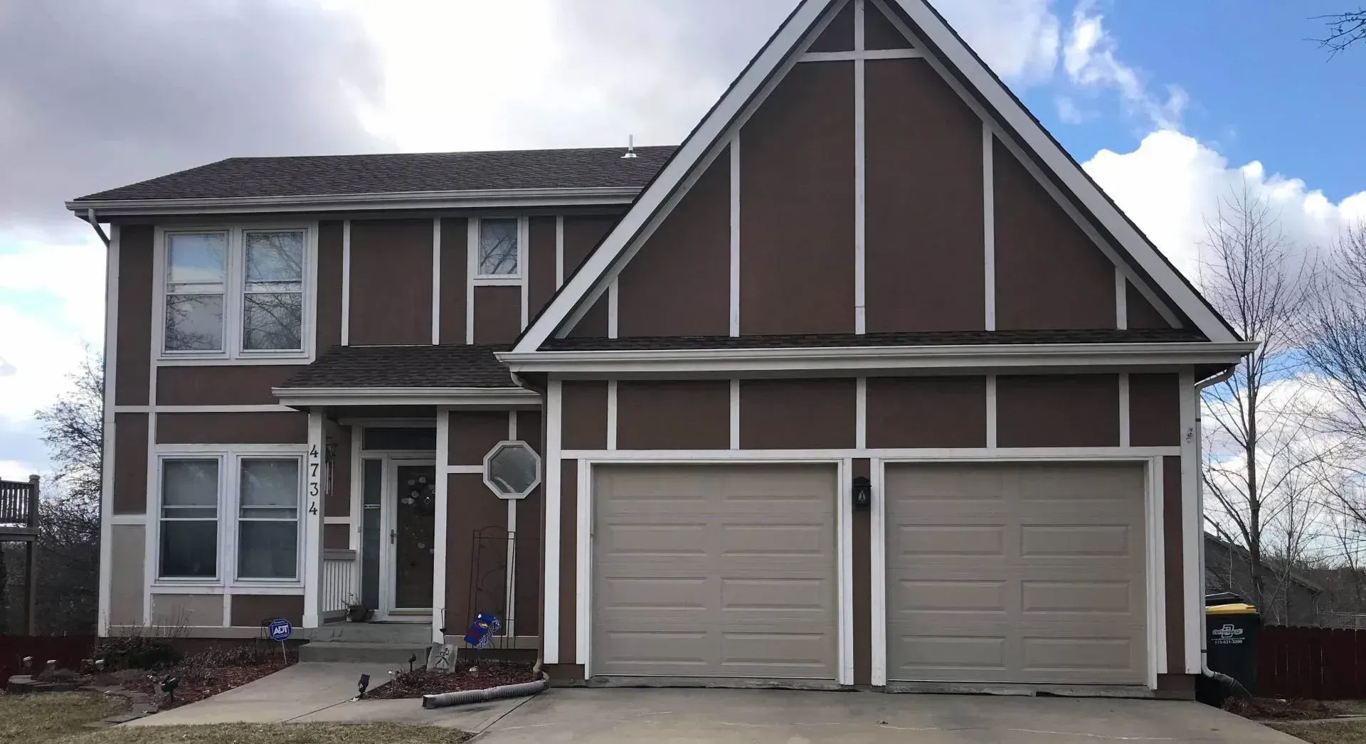 A brown house with a white trim and two garage doors.