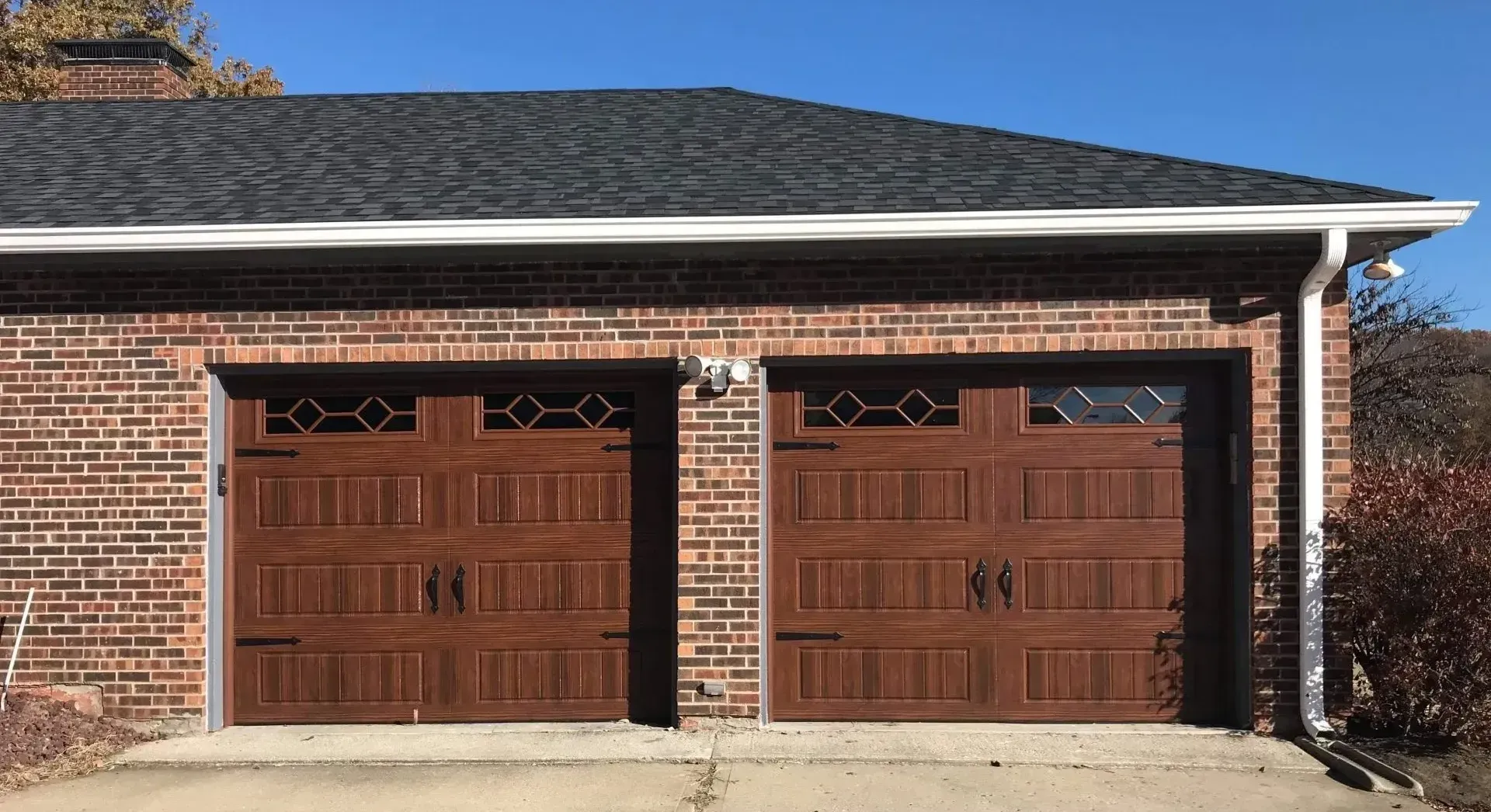 A brick garage with two brown garage doors and a black roof.