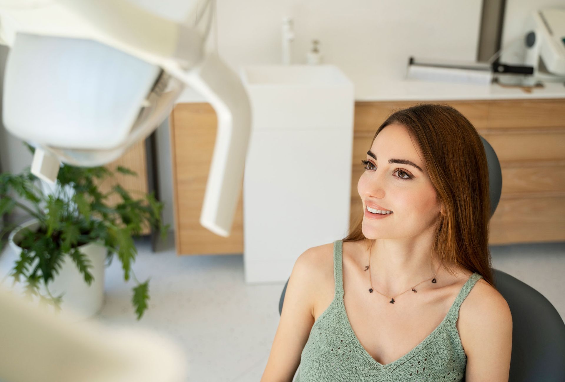 Woman in dental chair, looking up, smiling; dental office setting with equipment.