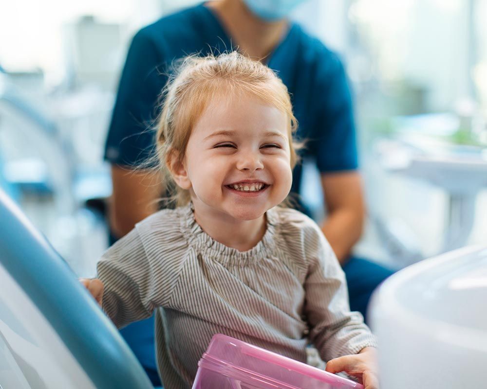 First children dental appointment - Smiling young girl sitting in a dental chair in her dentist's of