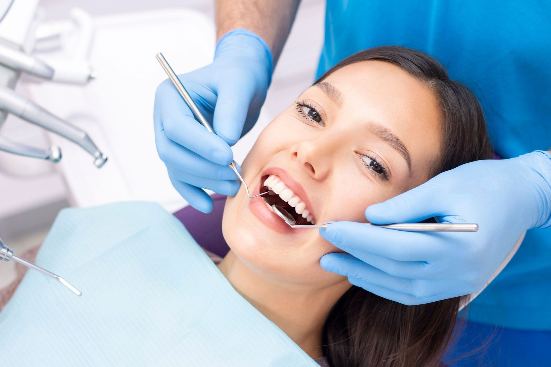 Woman at dentist, mouth open, being examined. Dentist in blue gloves holding tools.