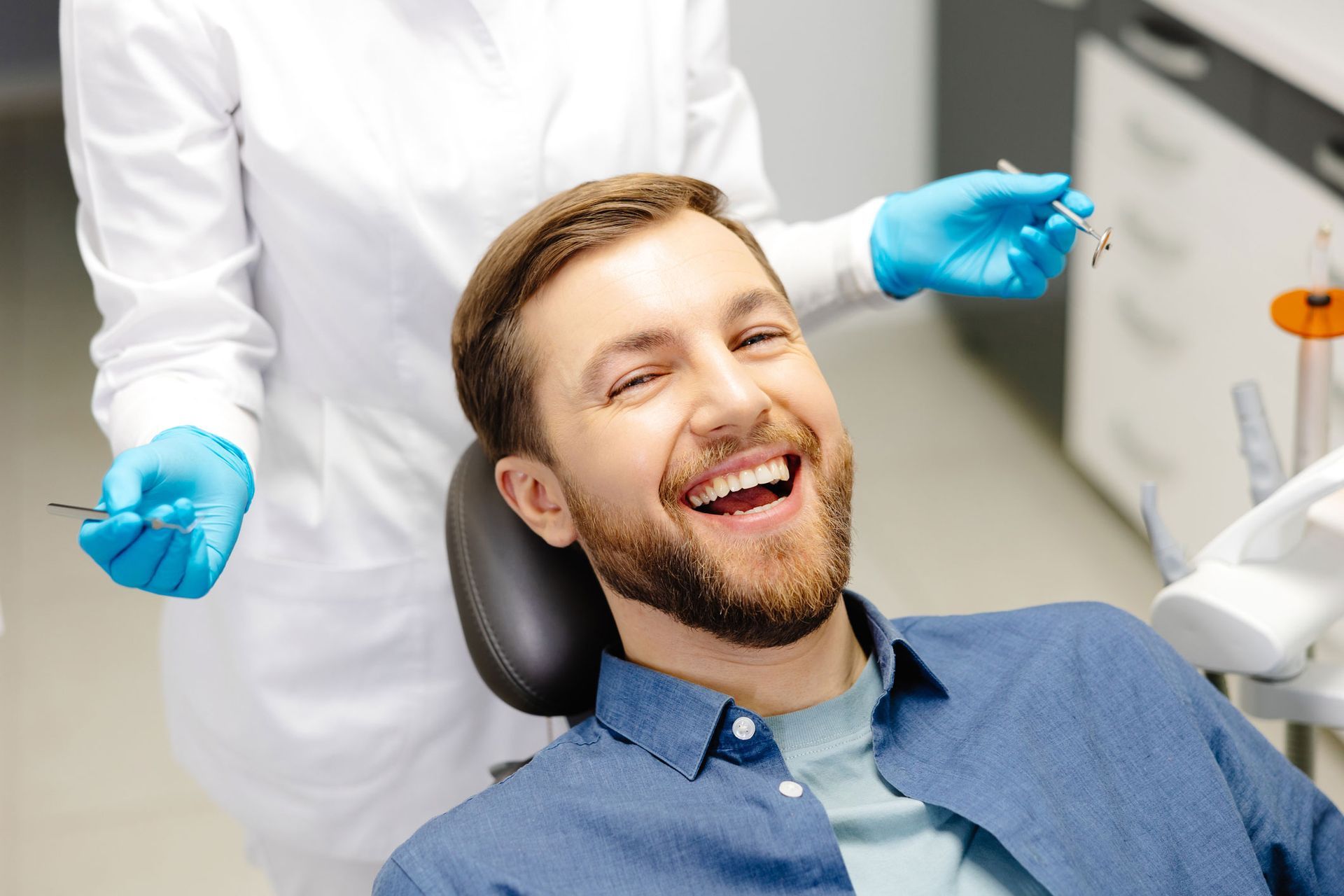 Man smiling widely in a dental chair; dentist in white coat holds tools in blue gloves.