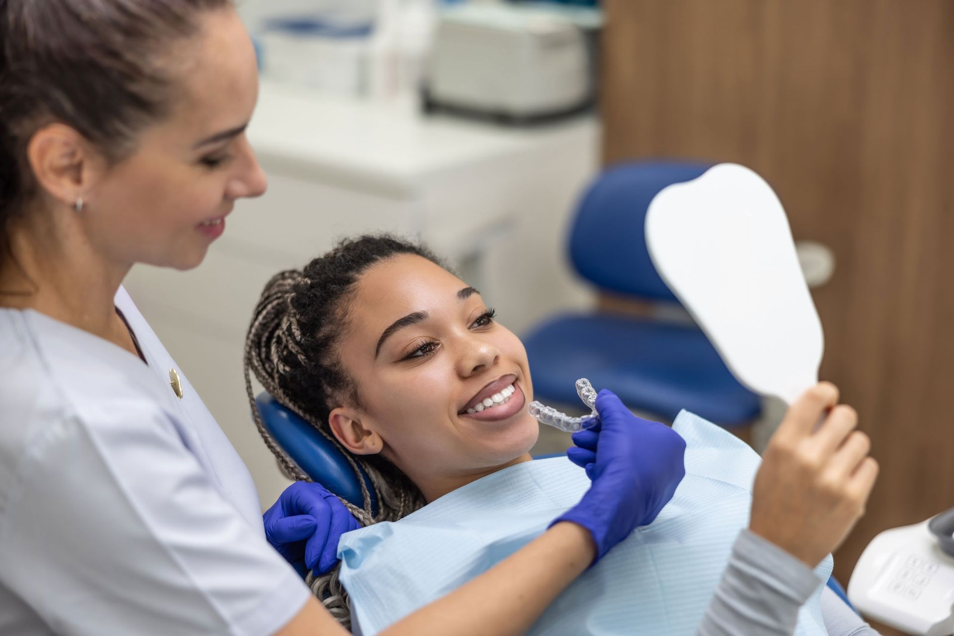 A female dentist shows her female patient her new smile in front of a hand mirror.