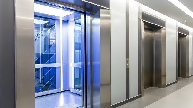 Modern office hallway with stainless steel elevators, one open with blue lighting and glass walls