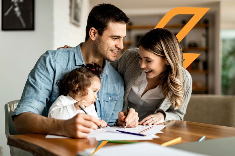 Familia de tres personas sentadas en una mesa dibujando juntos, sonriendo en un ambiente hogareño.