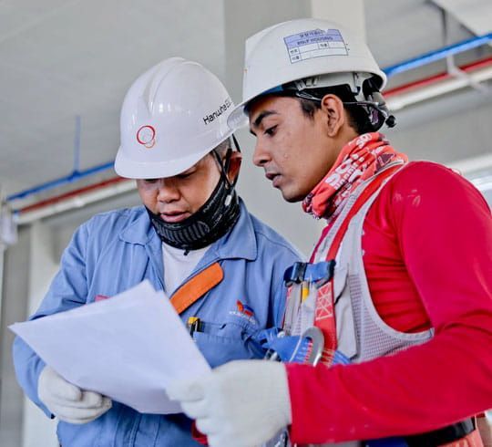 Obrero de la construcción subiendo una escalera, vistiendo un casco amarillo y un chaleco naranja, contra un cielo azul.