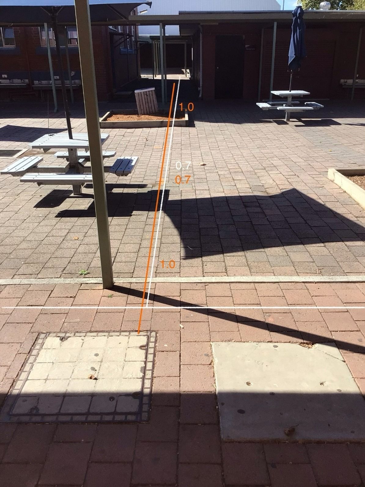 Brick patio with a pole casting a shadow, and two utility covers.