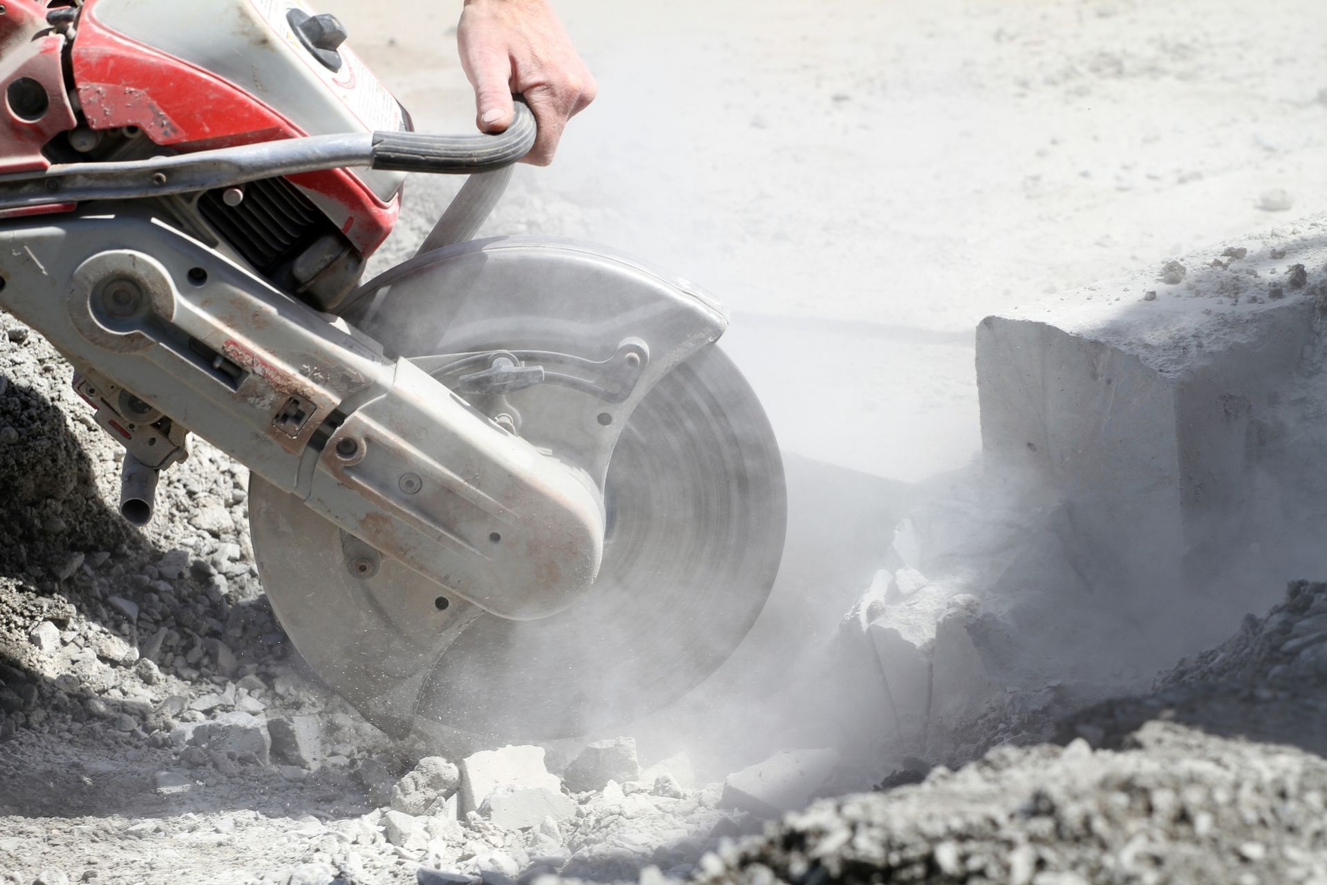 A person using a power saw to cut concrete, producing dust.