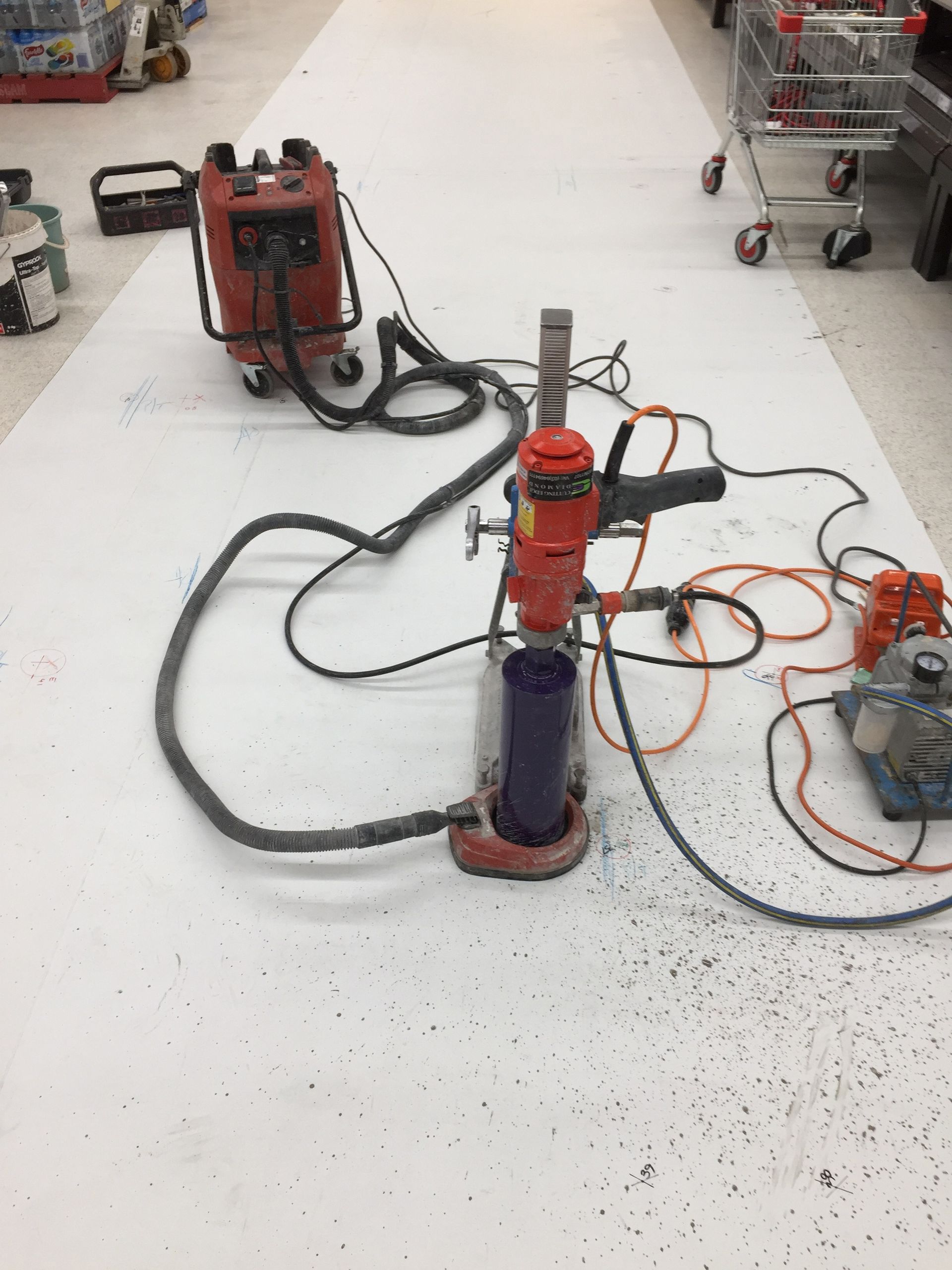 A core drill machine with connected vacuum is operating on a white surface in a retail store.
