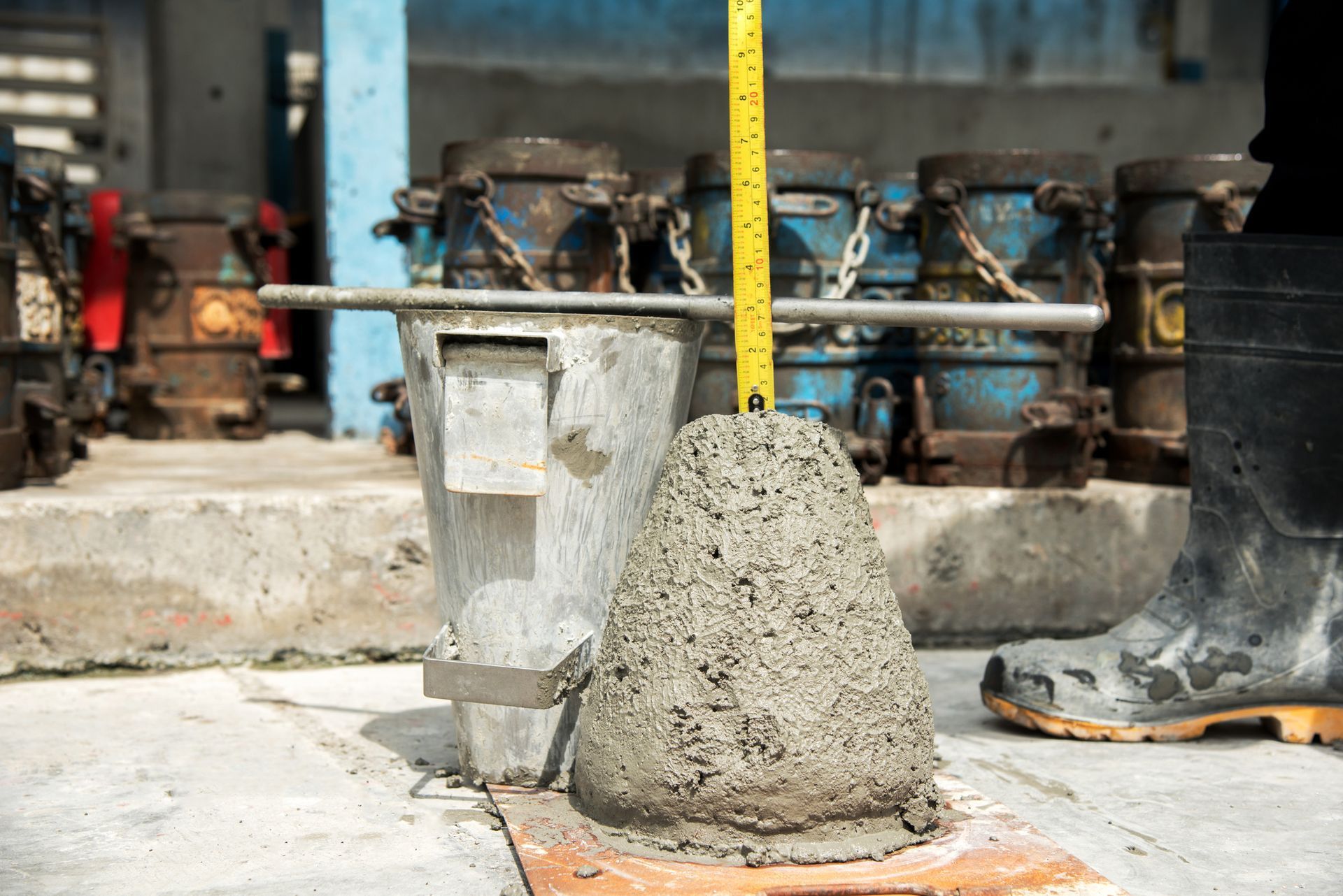 Concrete slump test in progress; concrete cone next to a measuring tape, metal molds in the background.
