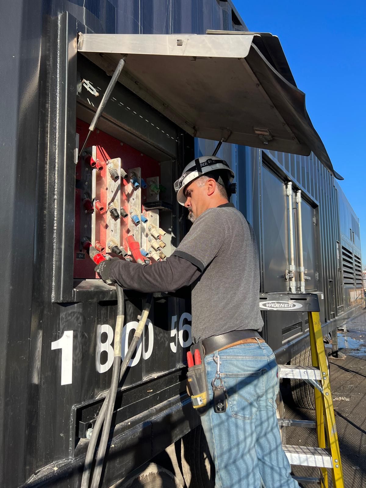 A railway worker in a hard hat repairs electrical components on a black train car.