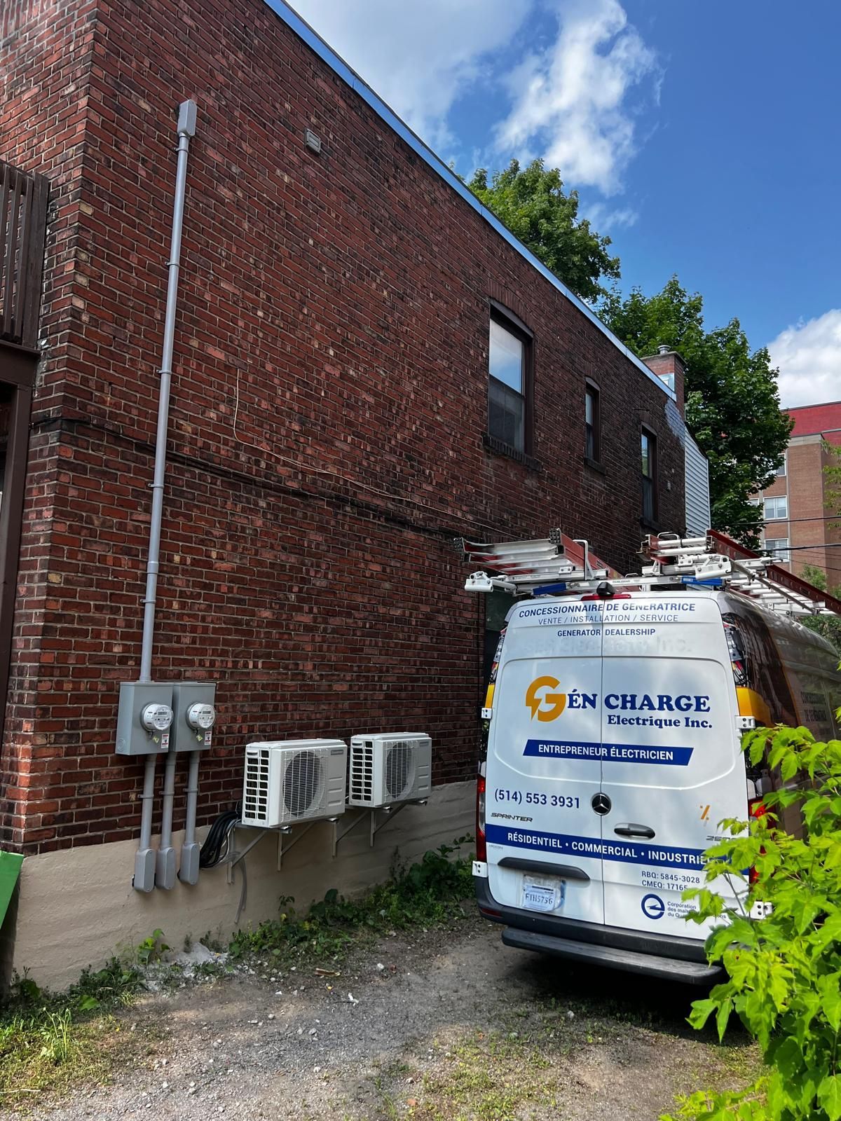 Brick building with a utility van parked beside it; air conditioning units and electrical equipment are visible.