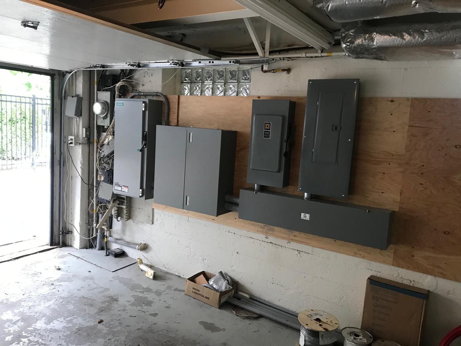 Garage interior with electrical panels and wiring on the wall, garage door open to the left.