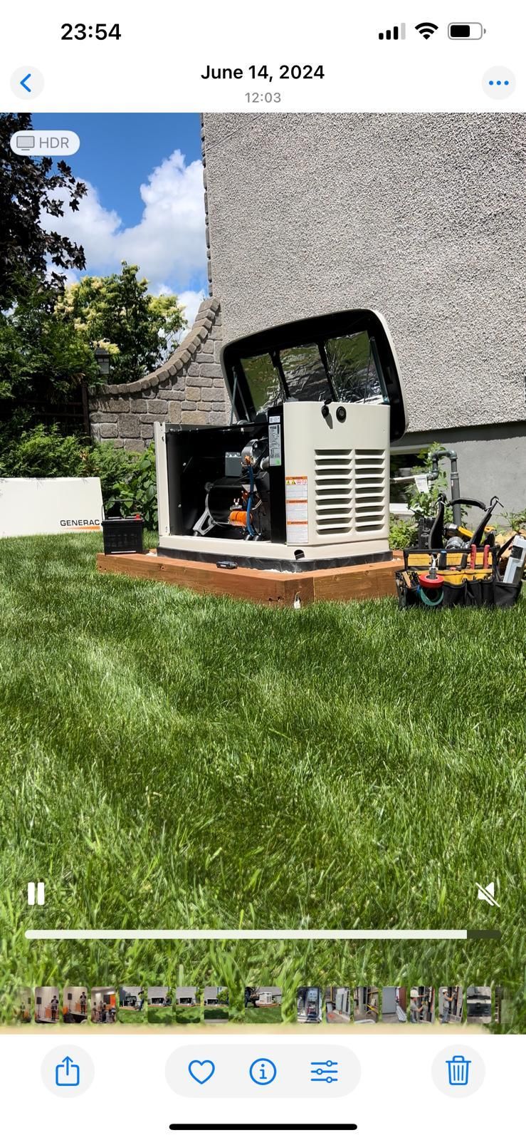 Générateur installé sur une base en briques brunes dans une cour arrière herbeuse avec un ciel bleu en arrière-plan.