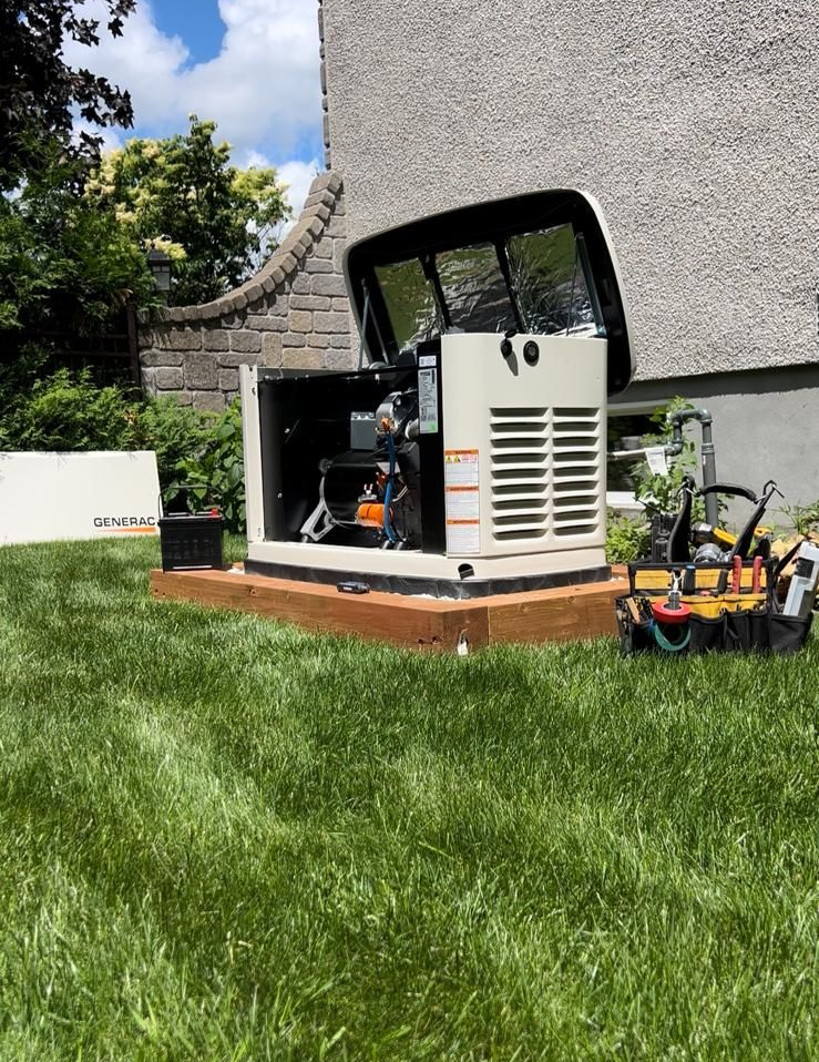 Generator installed next to a house with open lid; tools sit nearby on grass.