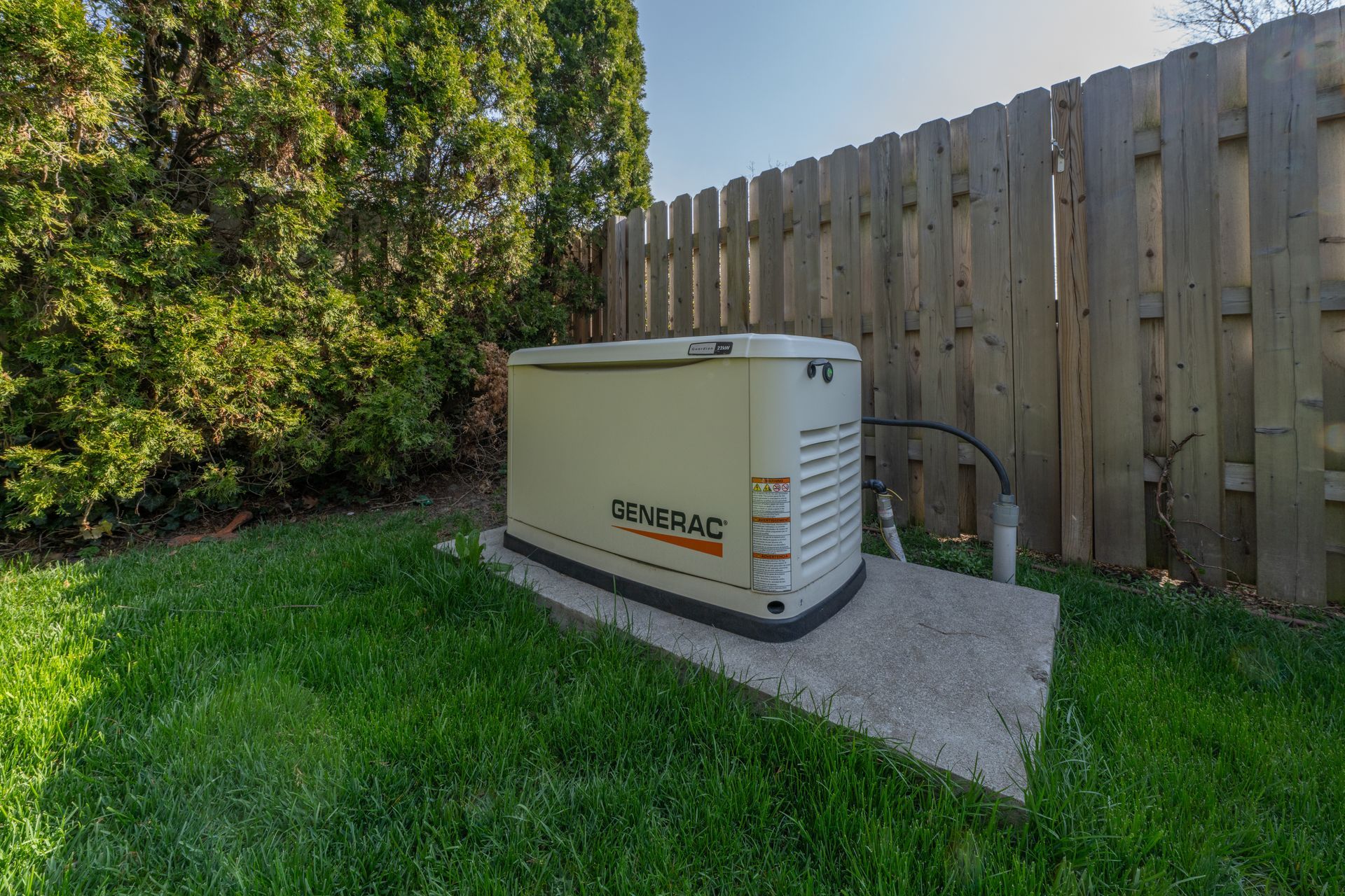 A beige Generac home generator on a concrete pad in a grassy backyard near a wooden fence.