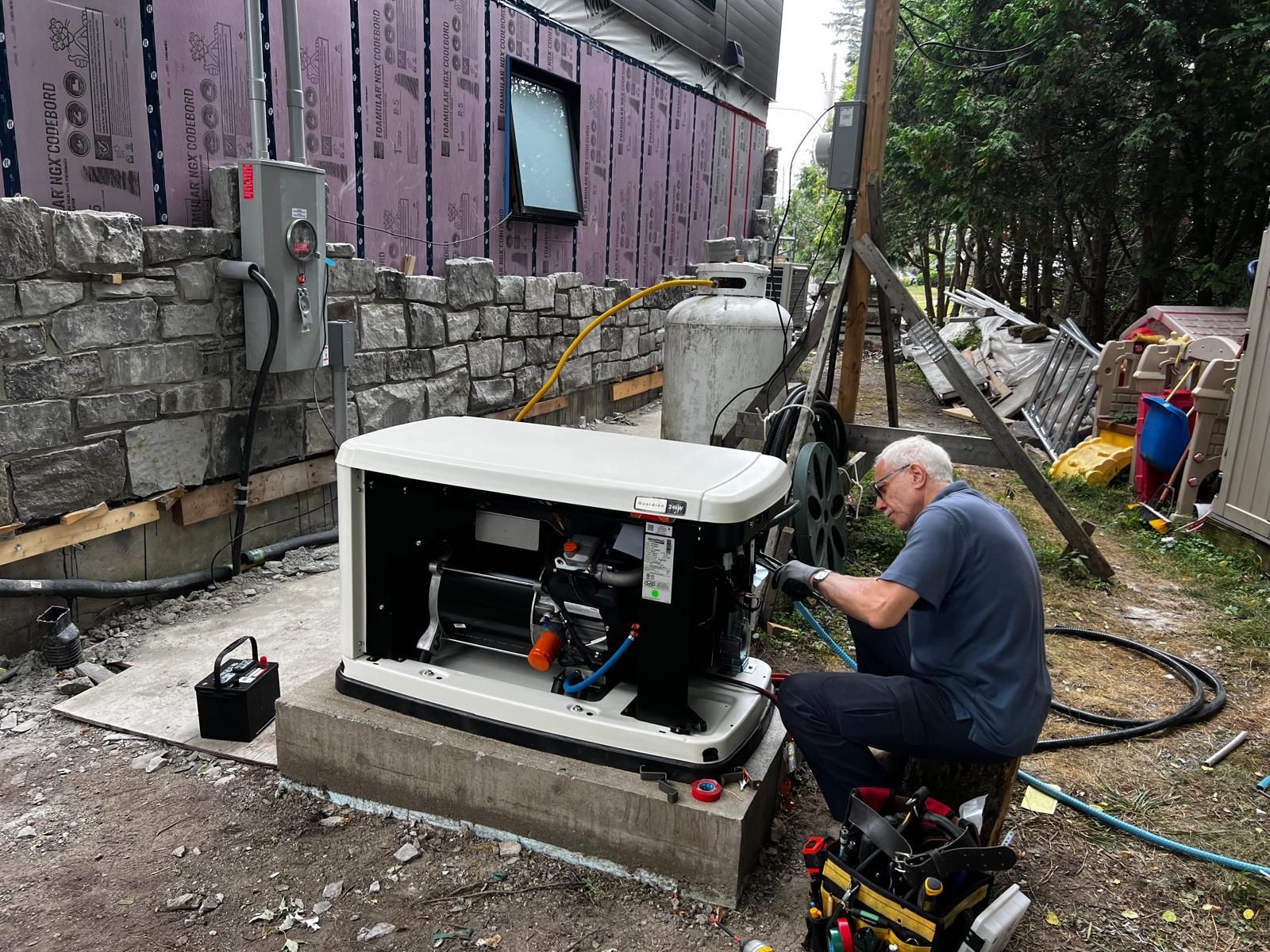 Man working on a generator outside a building. The generator is on a concrete pad, near a propane tank.