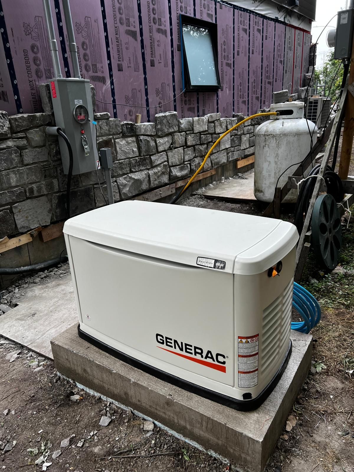 Generac generator on concrete base, with propane tank and electrical box. Exterior view.