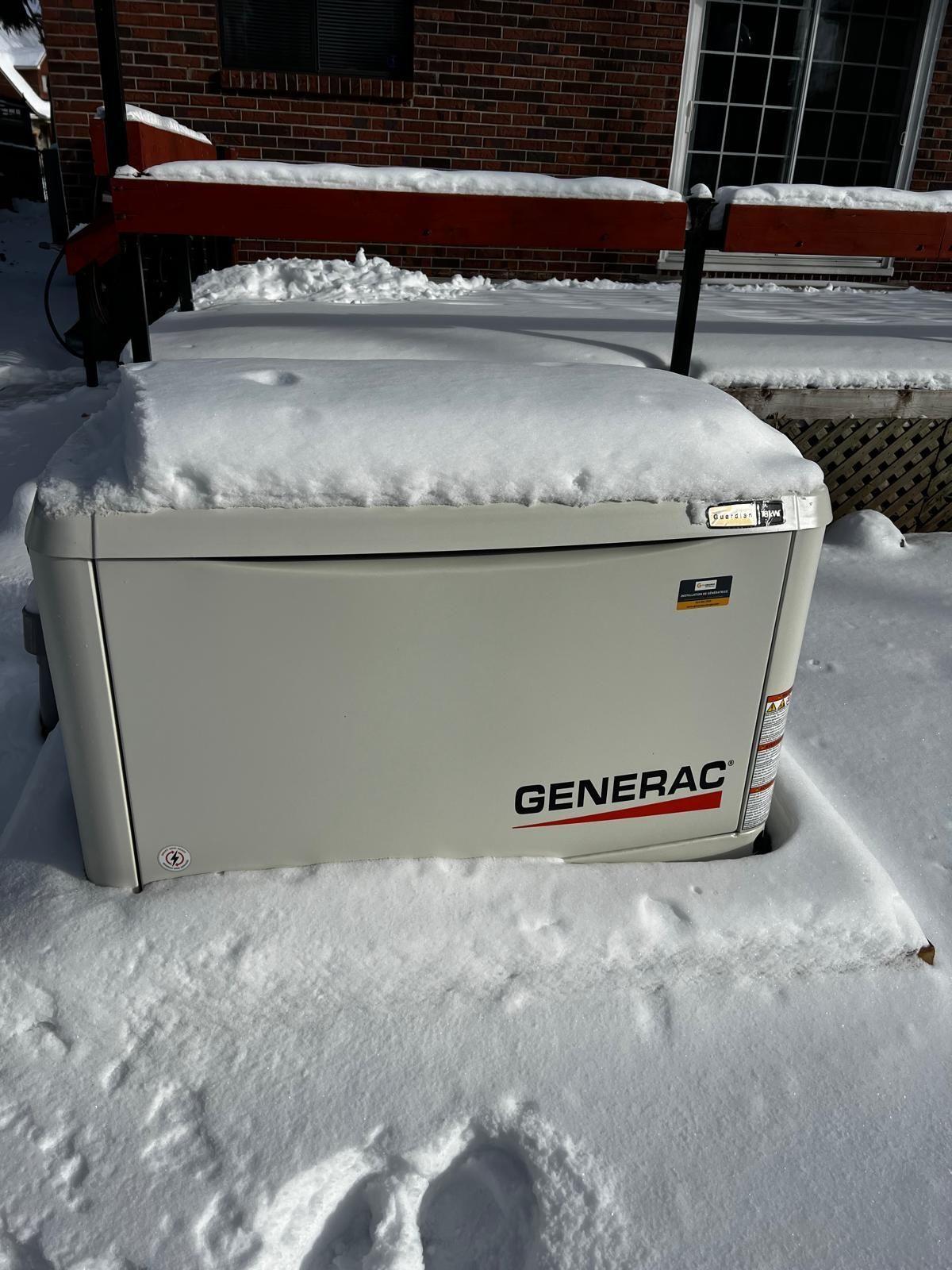 A snow-covered Generac generator sits outdoors.