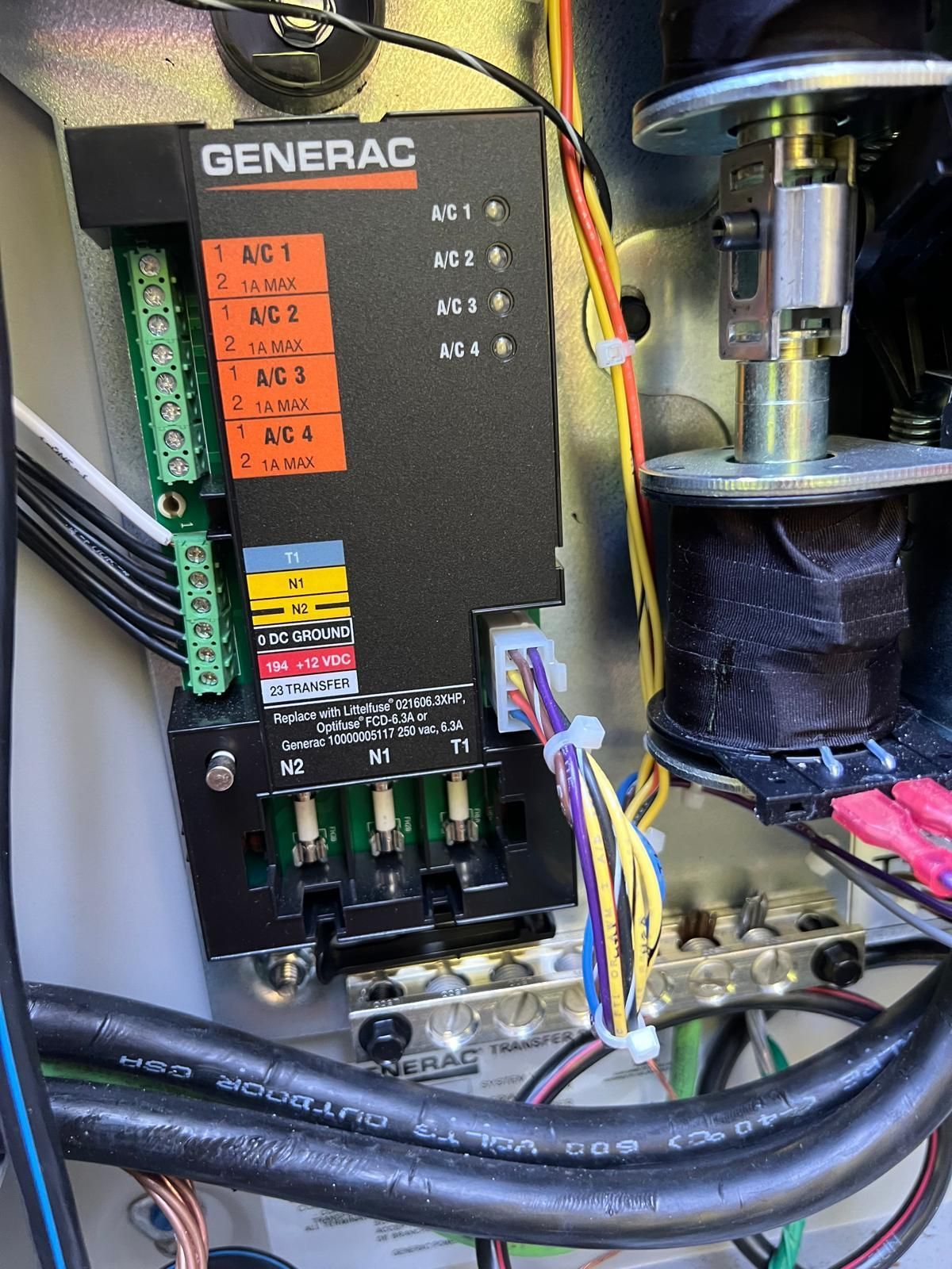 Generac generator control panel with wires, terminals, and a solenoid valve inside a metal enclosure. Orange and green labels are visible.