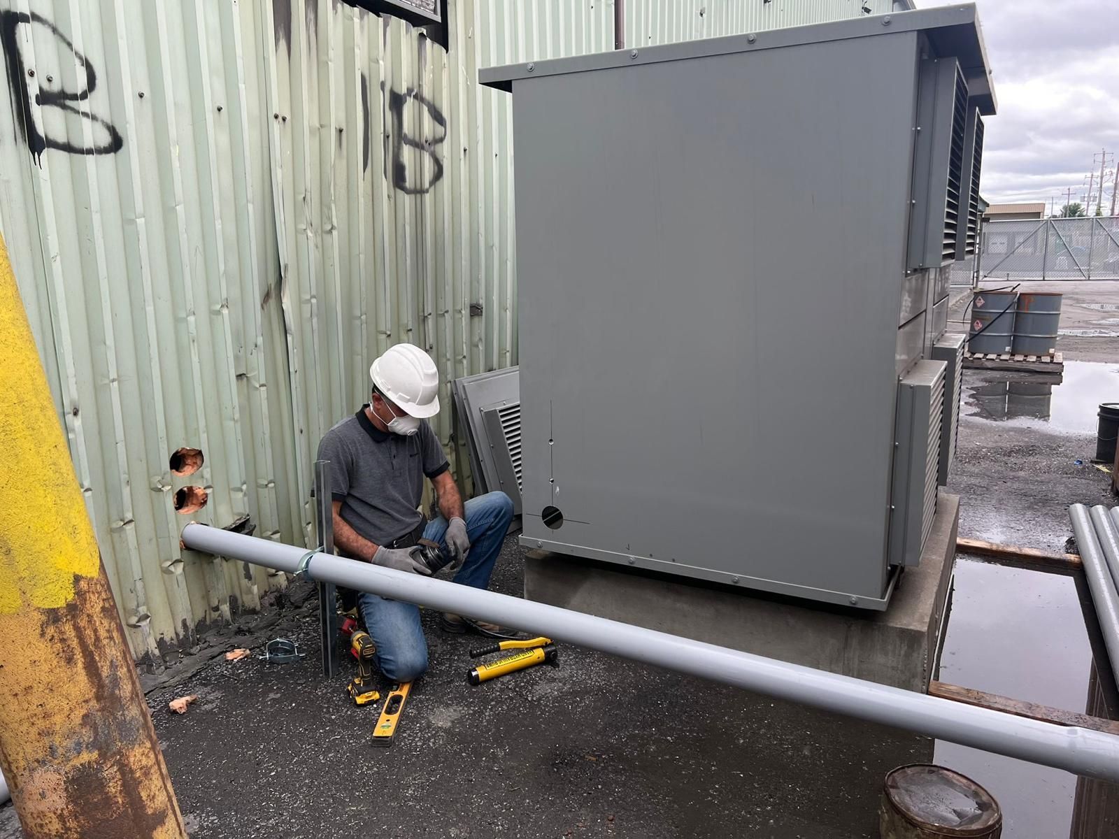 Construction worker in hard hat cutting conduit next to a gray electrical box and corrugated metal wall.