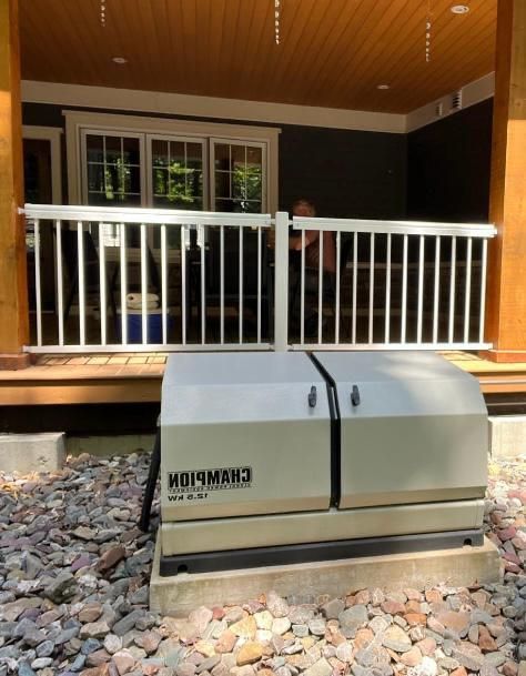 A beige Champion home generator sits on a gravel base near a porch with white railings. The background shows a house with windows and a wooden ceiling.