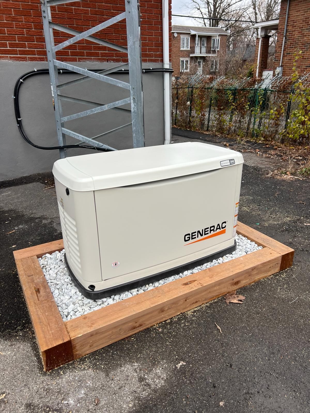 Un générateur Generac sur une plate-forme en bois avec gravier, à côté d'un bâtiment et d'une structure métallique.