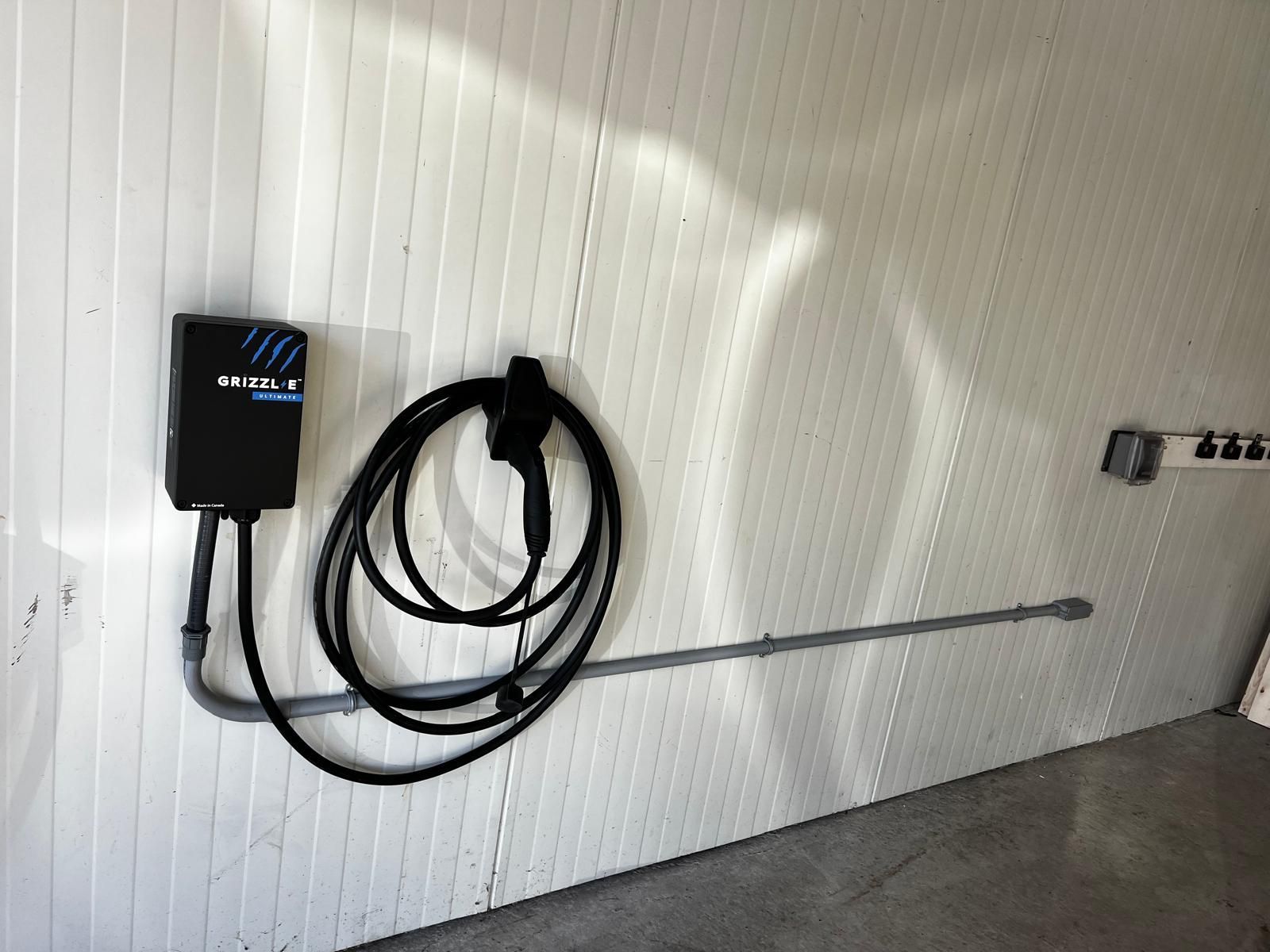 Chargeur de véhicule électrique monté sur un mur blanc, avec un câble de charge spiralé et une prise de courant.