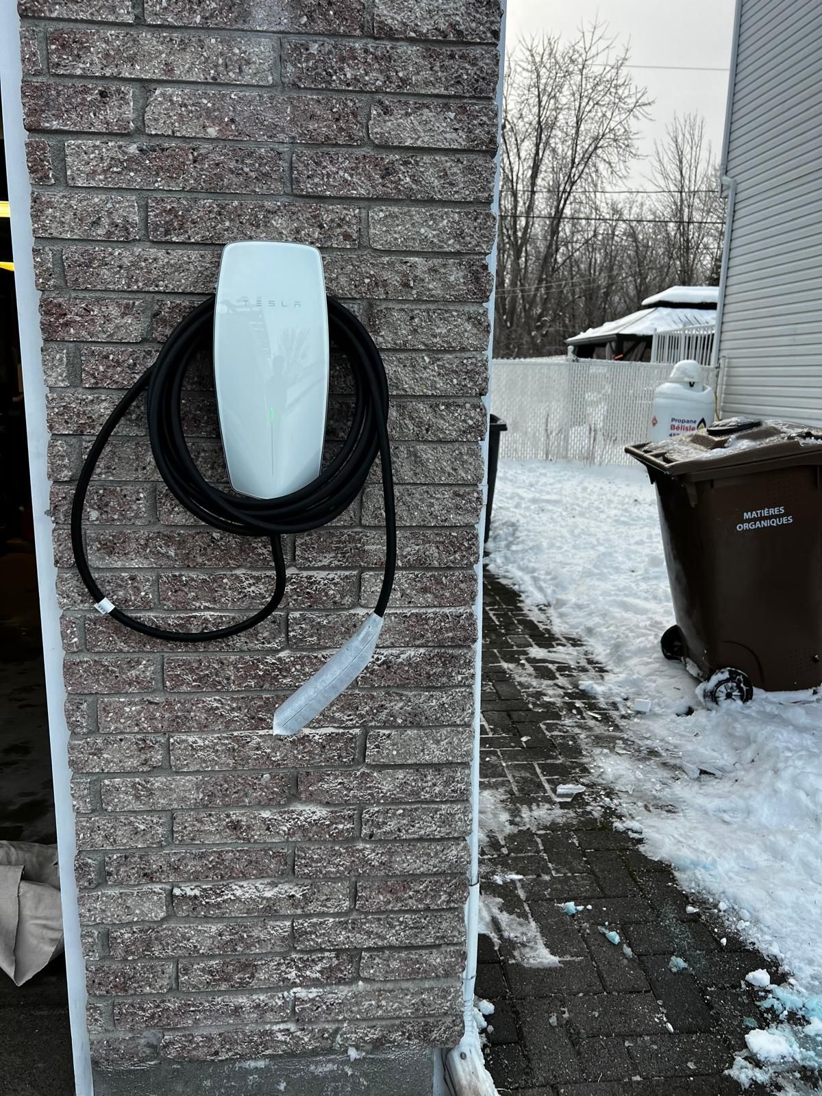 Chargeur de véhicule électrique monté sur un pilier en brique, avec câble de charge enroulé. Neige au sol.
