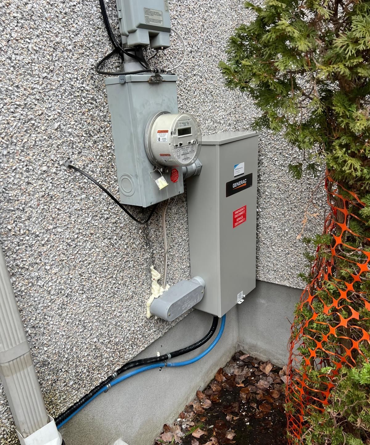 Exterior electrical panel and meter on a stucco building. Gray metal boxes house the meter, circuit breaker, and wiring.