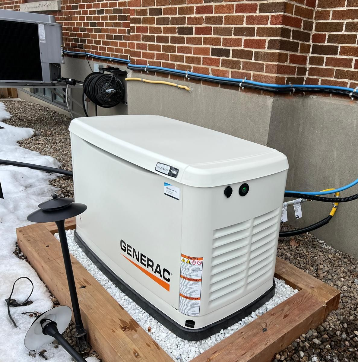 Generac generator on a gravel base next to a brick building.