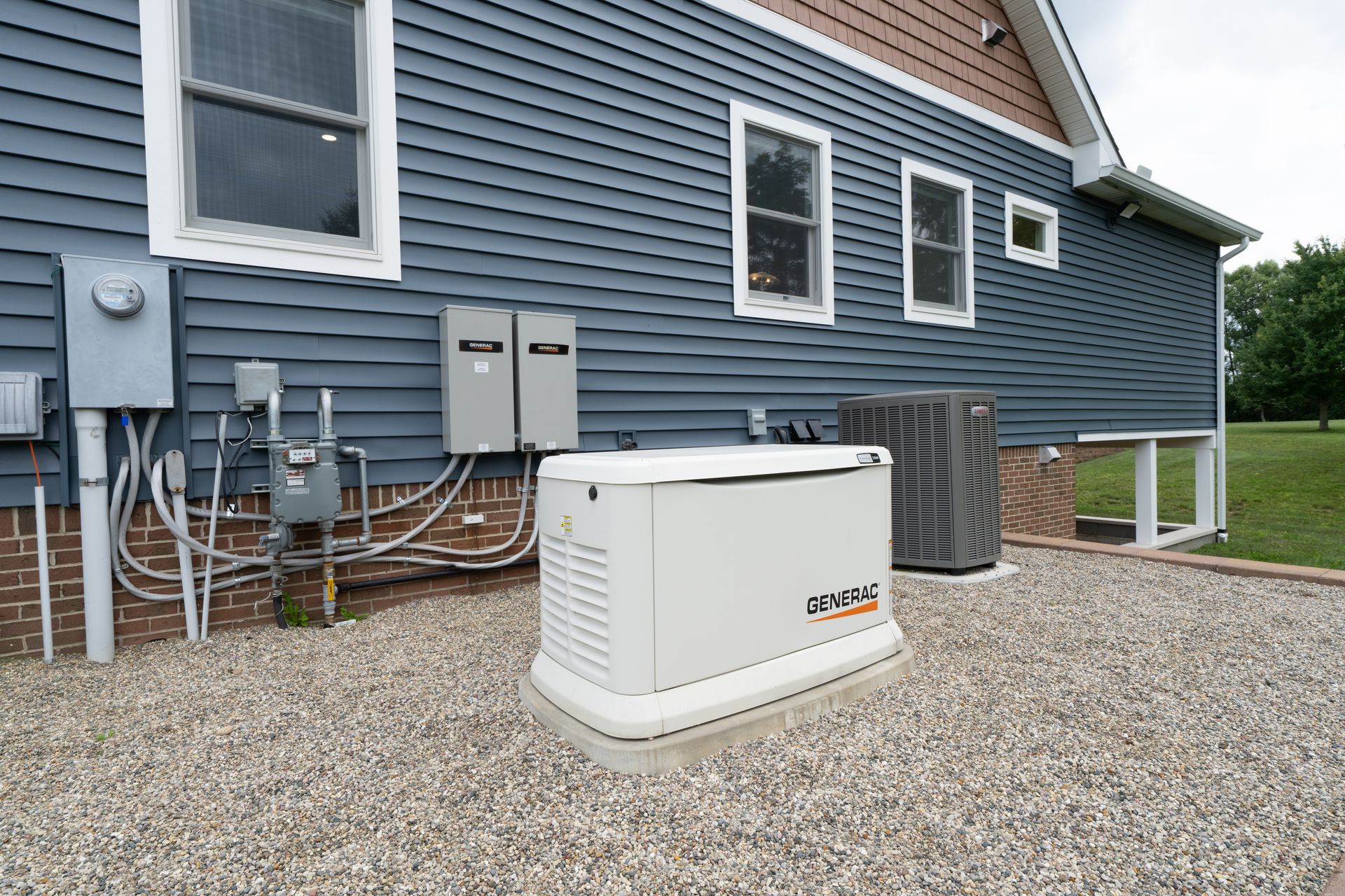 Exterior of a house with blue siding. Generator, electrical boxes, and air conditioning unit sit on gravel next to the wall.