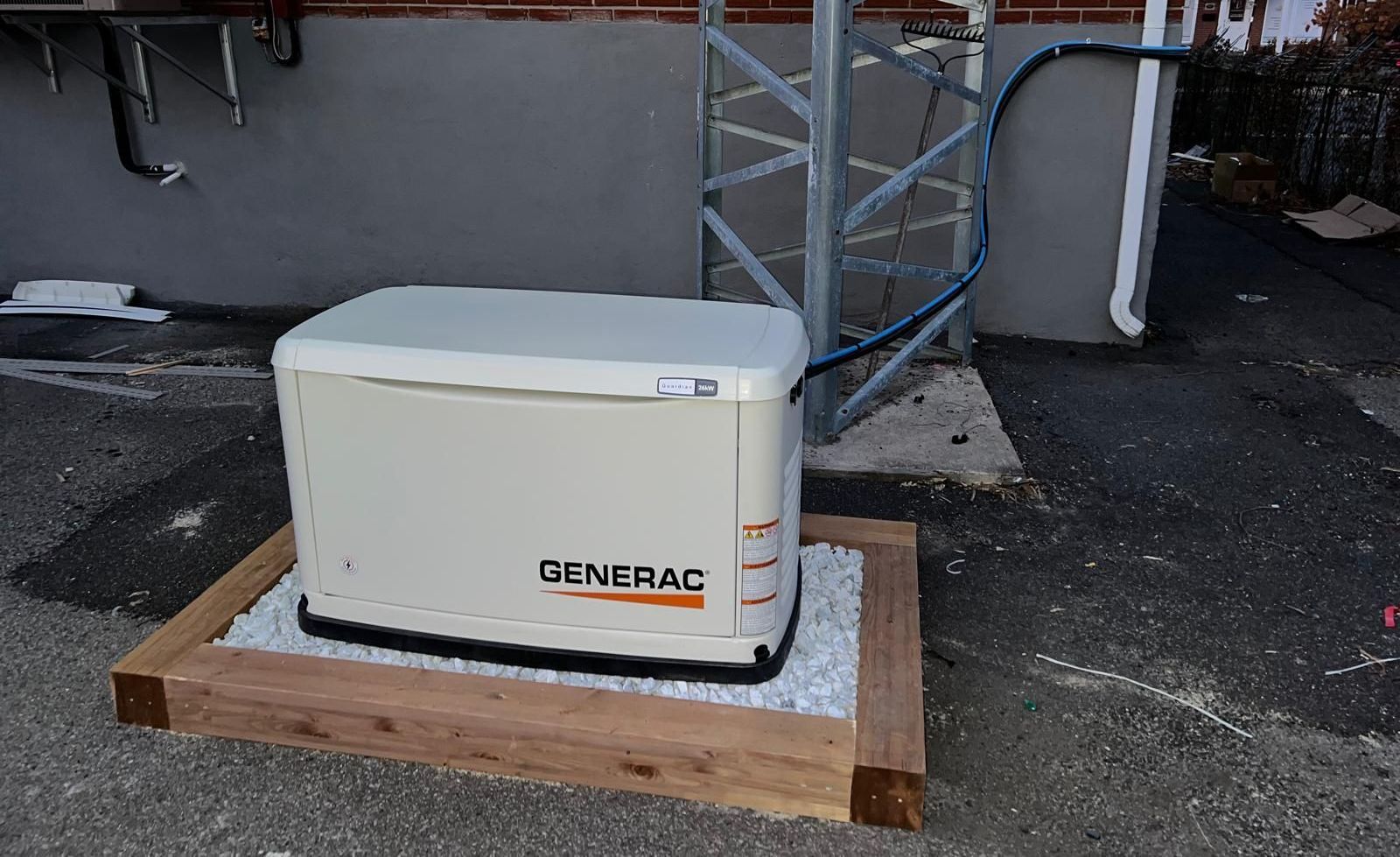 Generac generator on a wooden frame, next to a building, outside.
