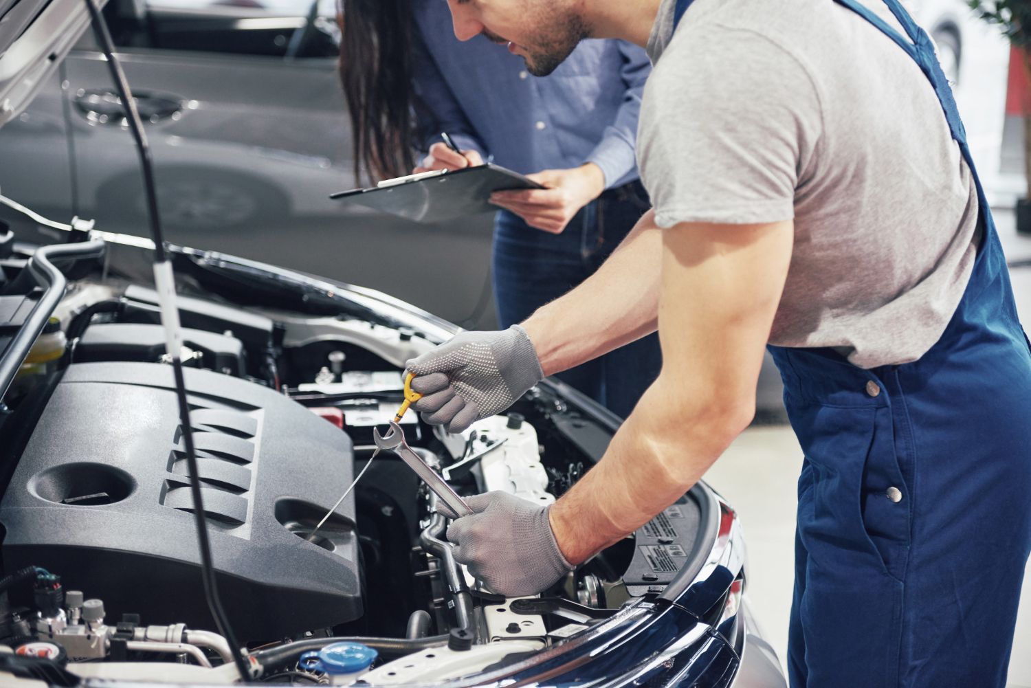 A man and a woman are working on a car in a garage.