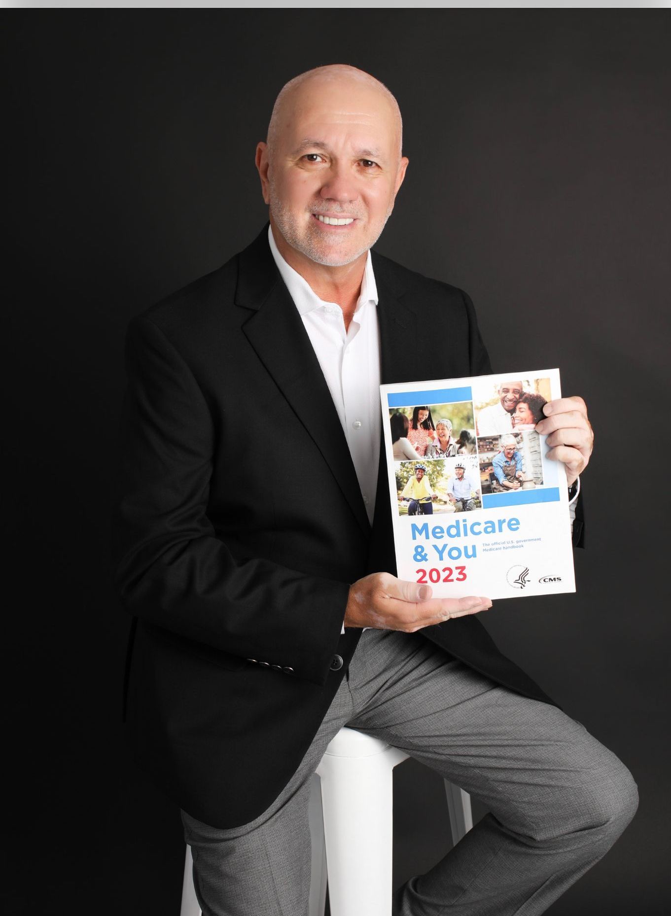 A man is sitting on a stool holding a book about medicare and you.