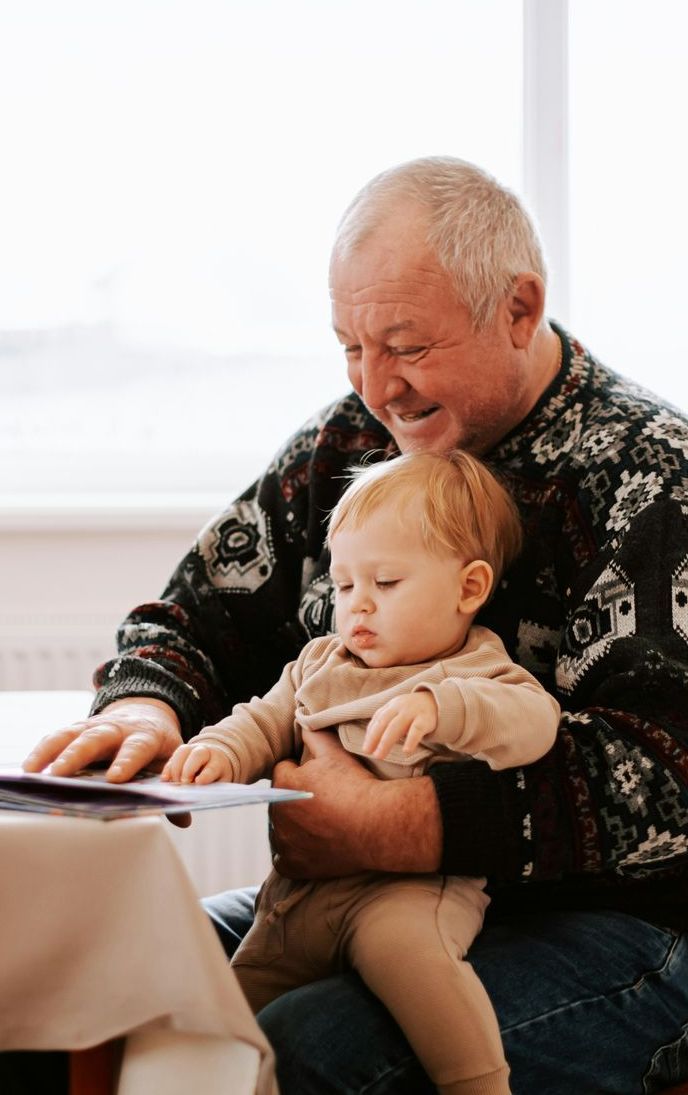 An elderly man is holding a baby while sitting at a table.