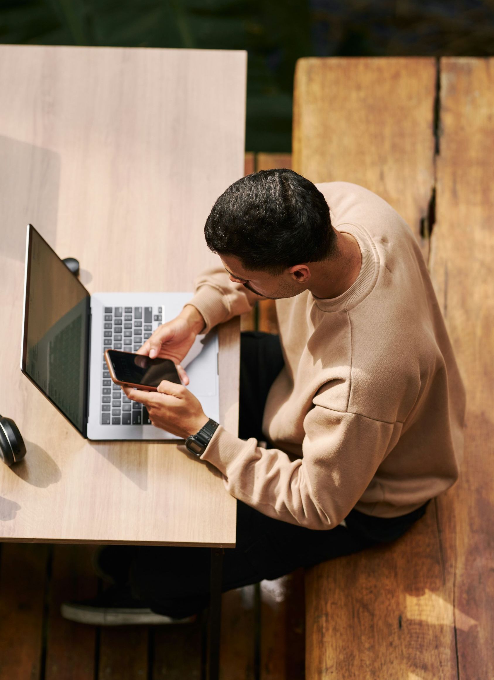A man is sitting at a table using a laptop and a cell phone.