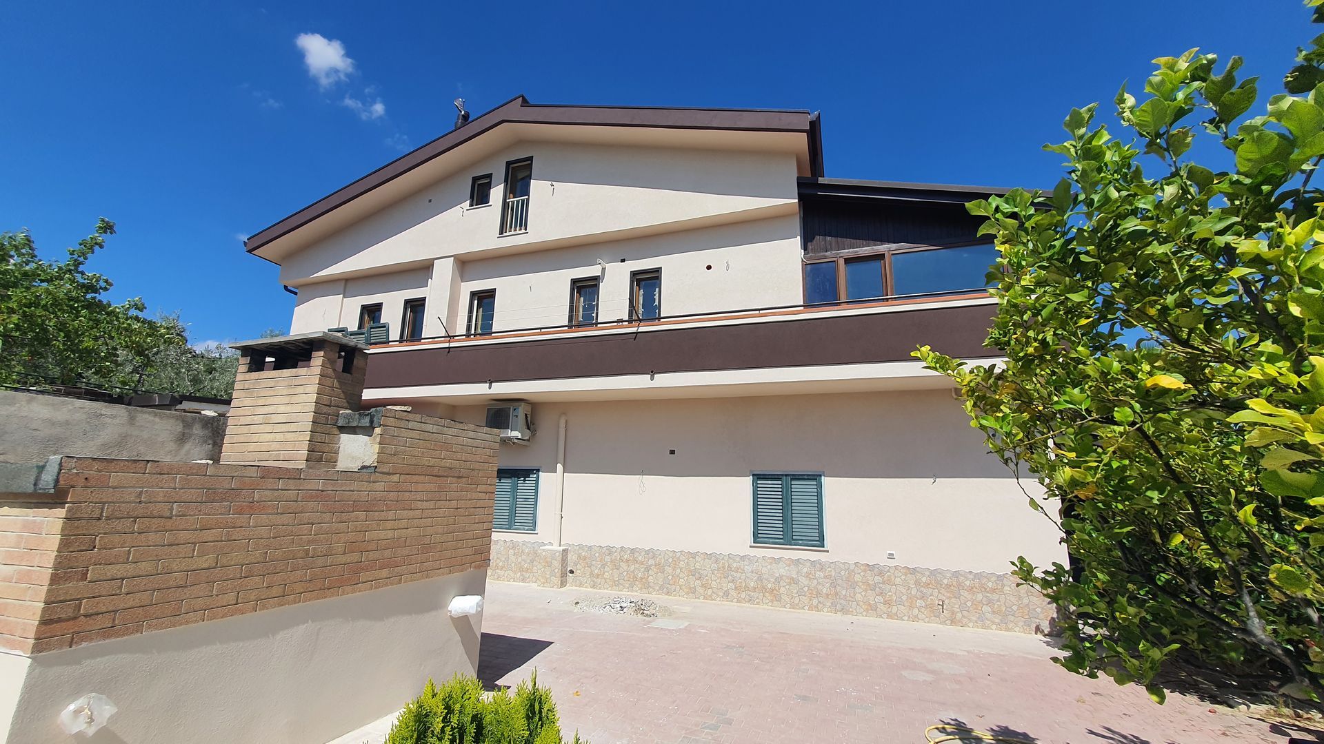 Una grande casa bianca con il tetto marrone è circondata da alberi.