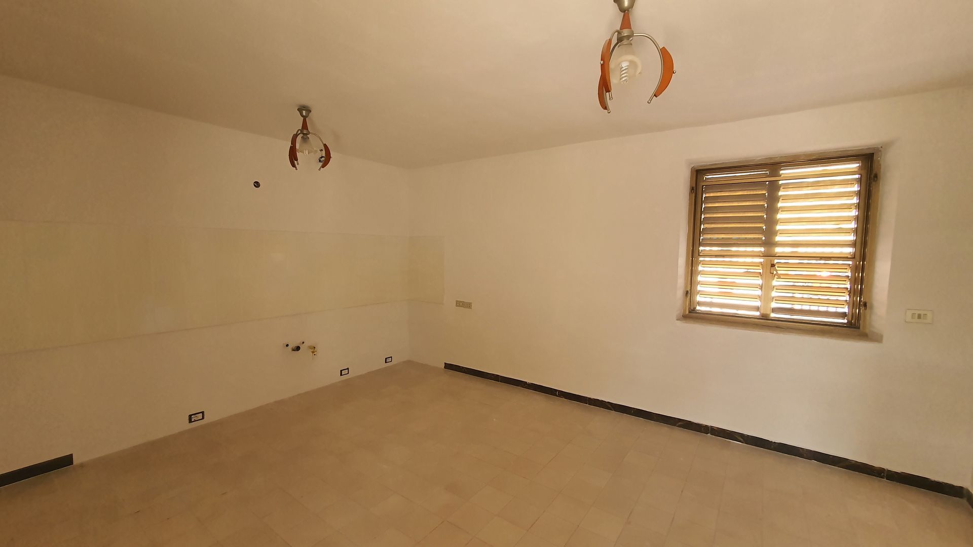 Una stanza vuota con una finestra e un lampadario appeso al soffitto.