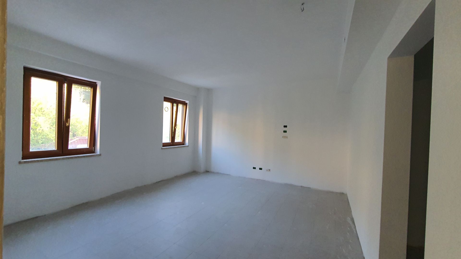 Una grande stanza vuota con due finestre e una porta.