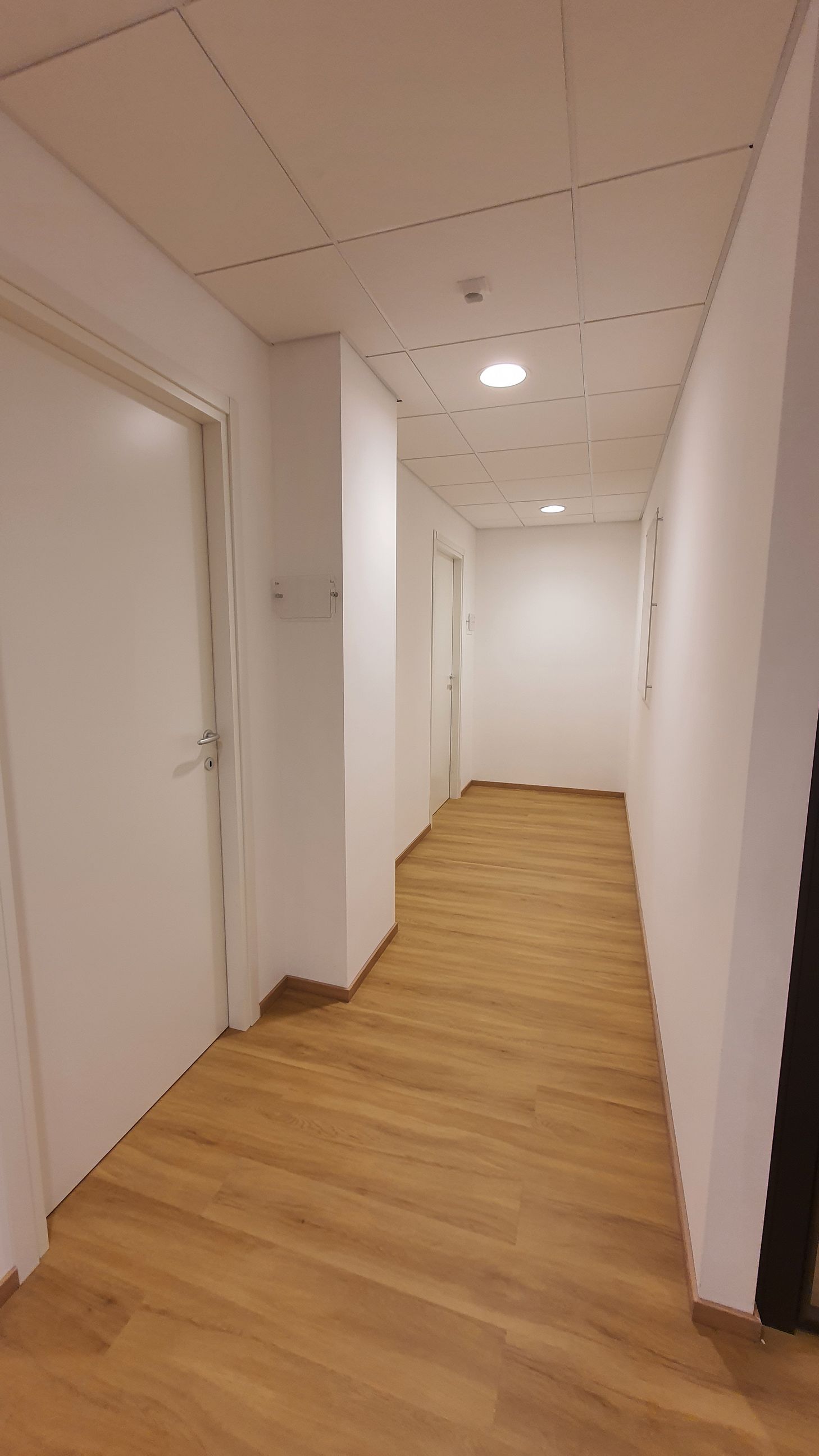 Un lungo corridoio con pavimenti in legno e pareti bianche.