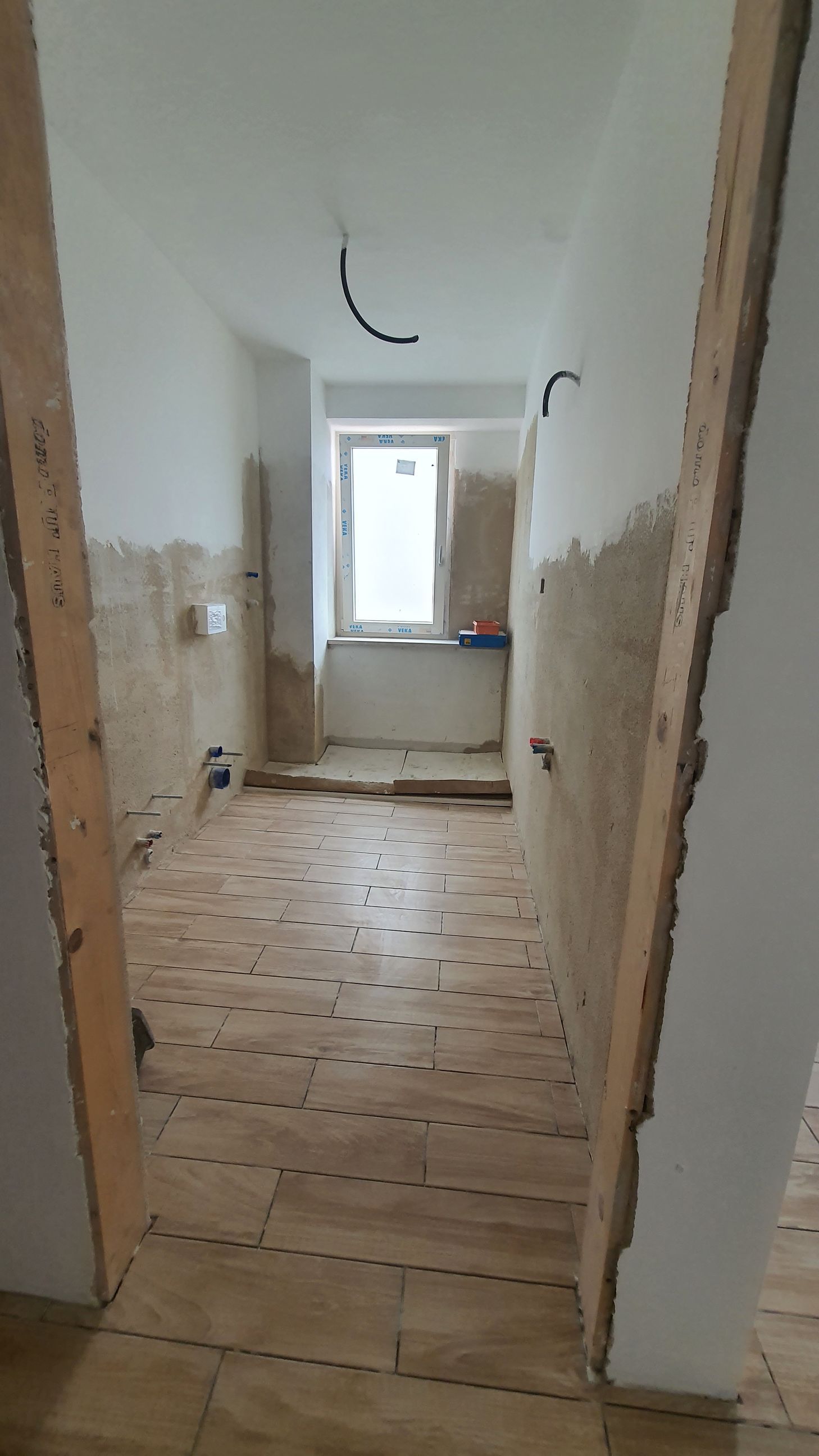 Un corridoio con pavimento in legno e una finestra in una casa in costruzione.