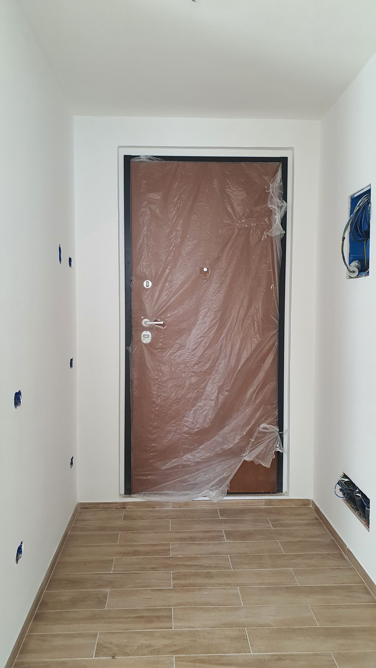 Un corridoio con una porta rivestita di plastica e un pavimento di legno.