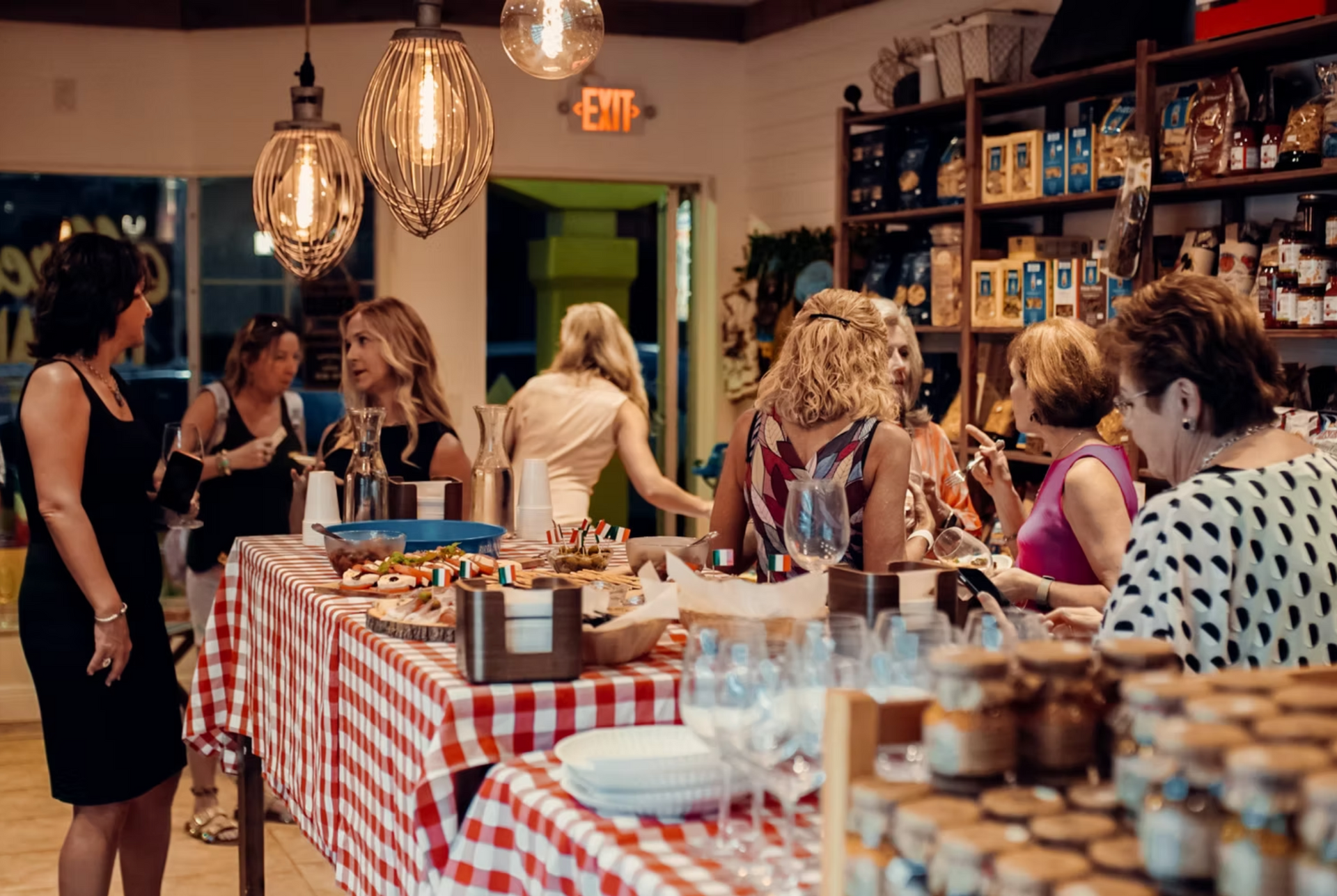 A group of women at a catered event in a shop, gathered around a buffet table with food and drinks.