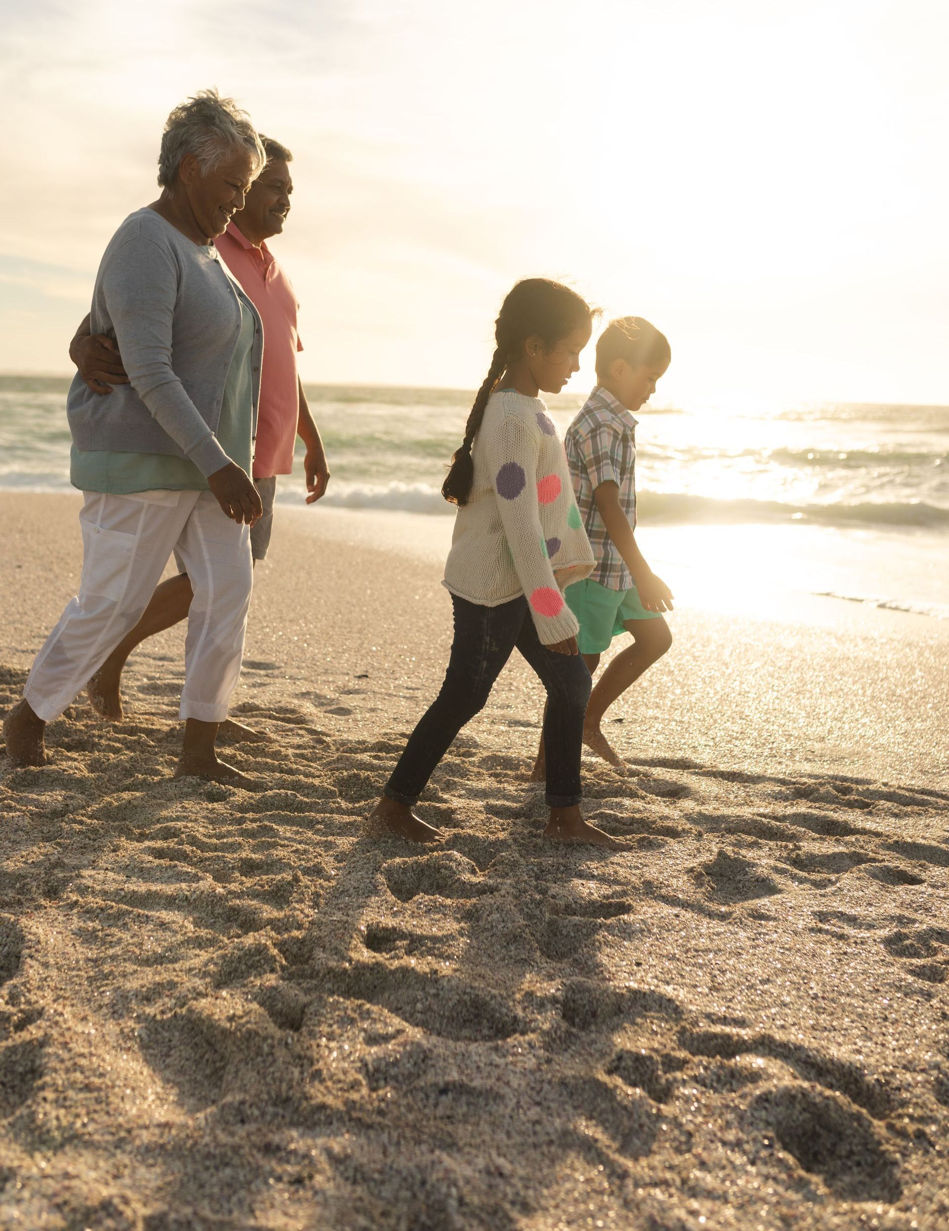 Family walking on a sandy beach at sunset; two grandparents with grandchildren.